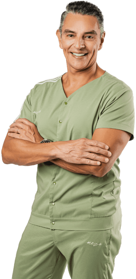 Dr. Meza poses for the camera crossing his arms and smiling, wearing a light green uniform.