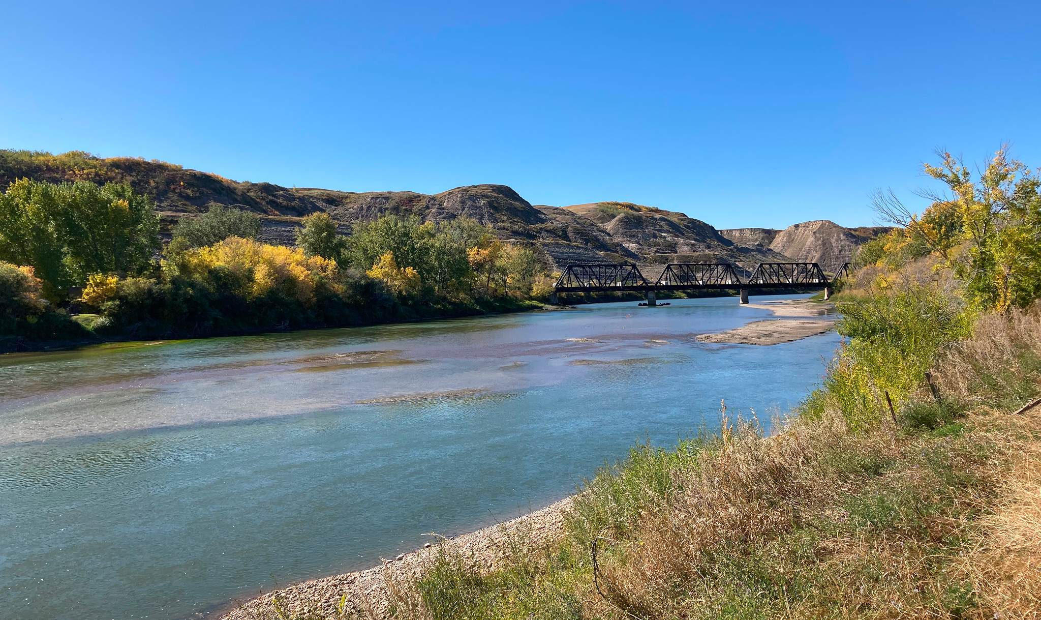 Red Deer River with railway bridge and autumn riparian vegetation along badlands in Drumheller