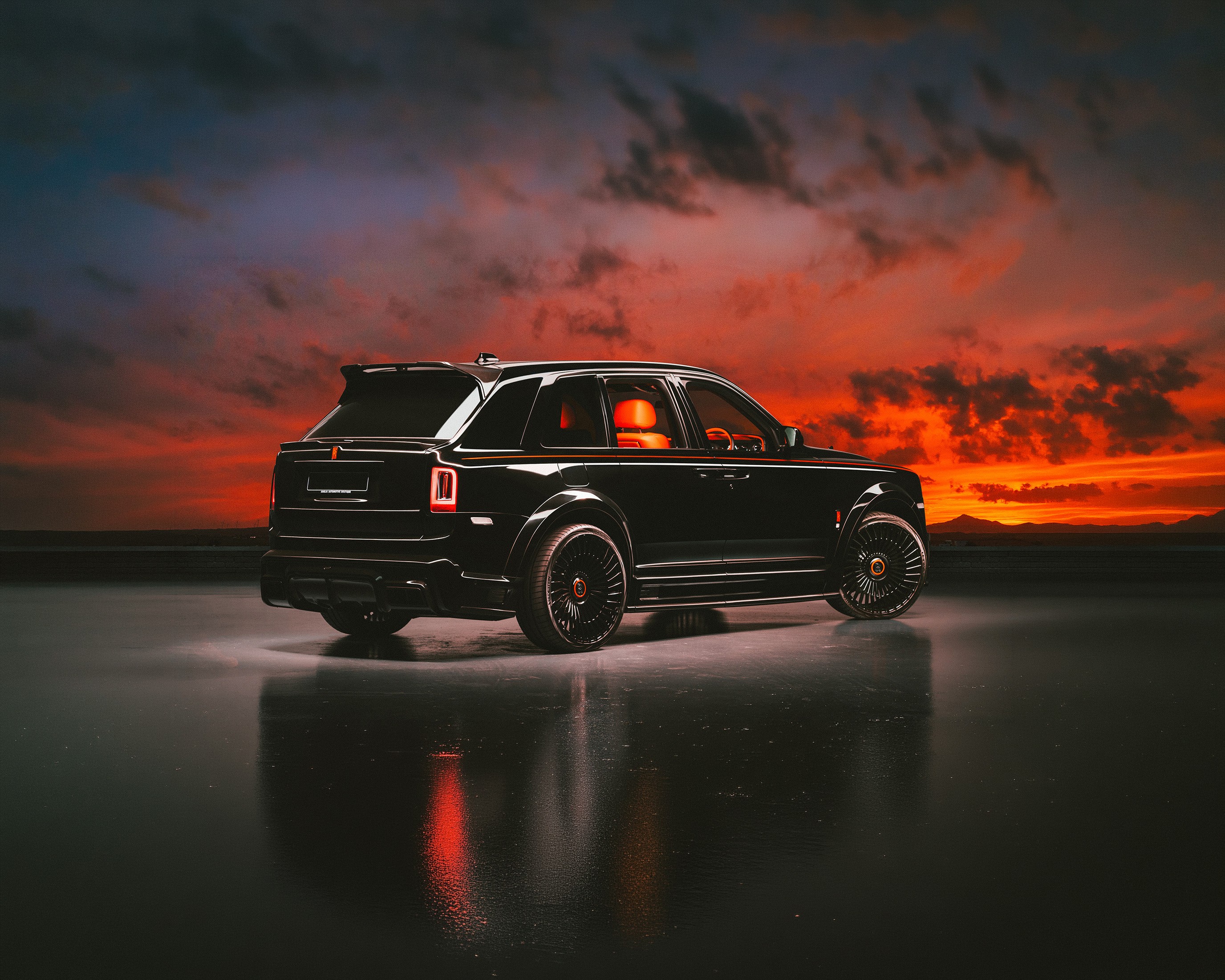 Black Rolls-Royce Cullinan modified by Urban Automotive, shown in rear three-quarter view with orange leather interior visible through the windows, an orange coachline along the body, and black turbine-style wheels, set against a deep orange sunset sky on a reflective floor.