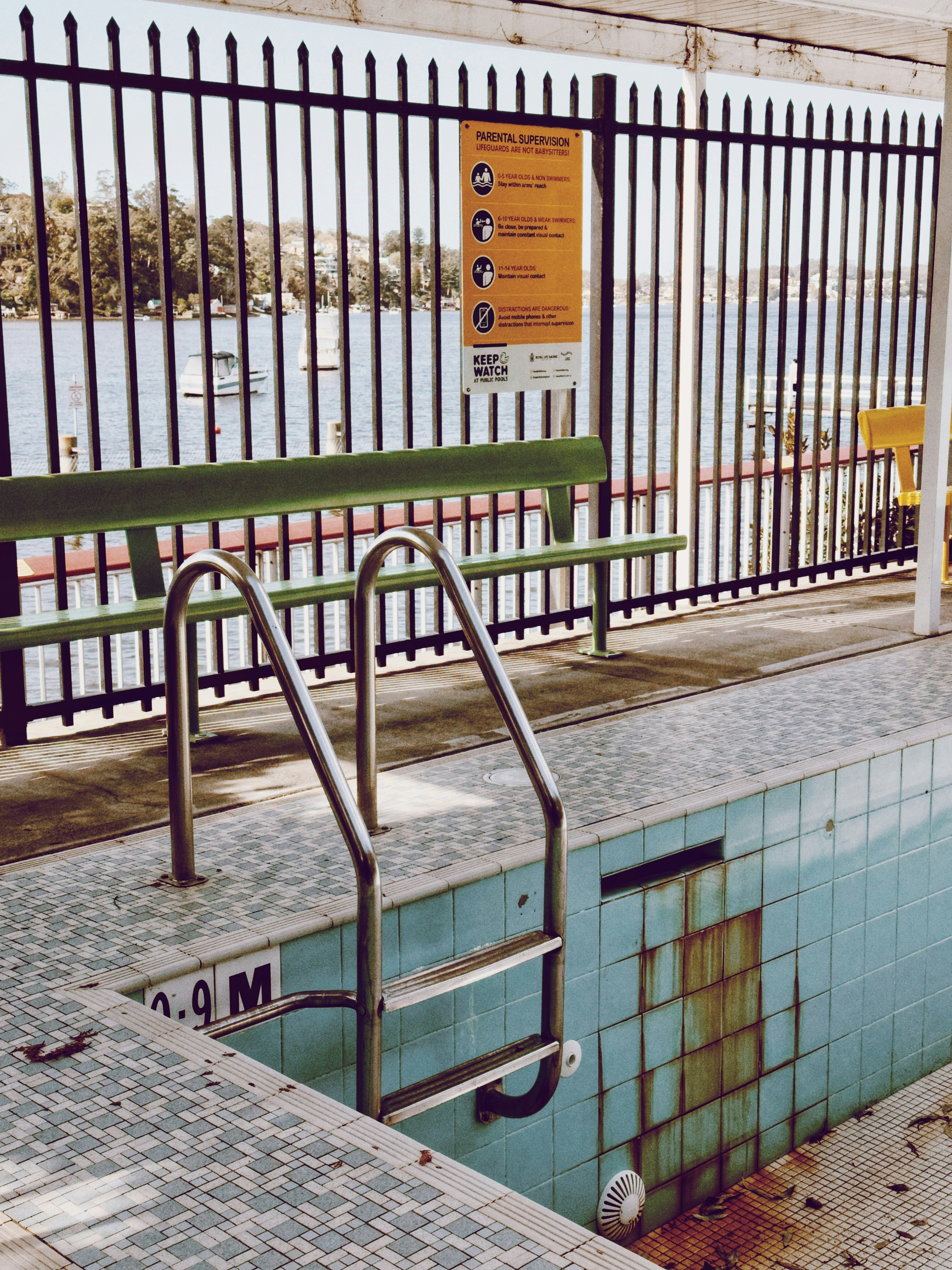 Empty swimming pool with metal ladder and fence