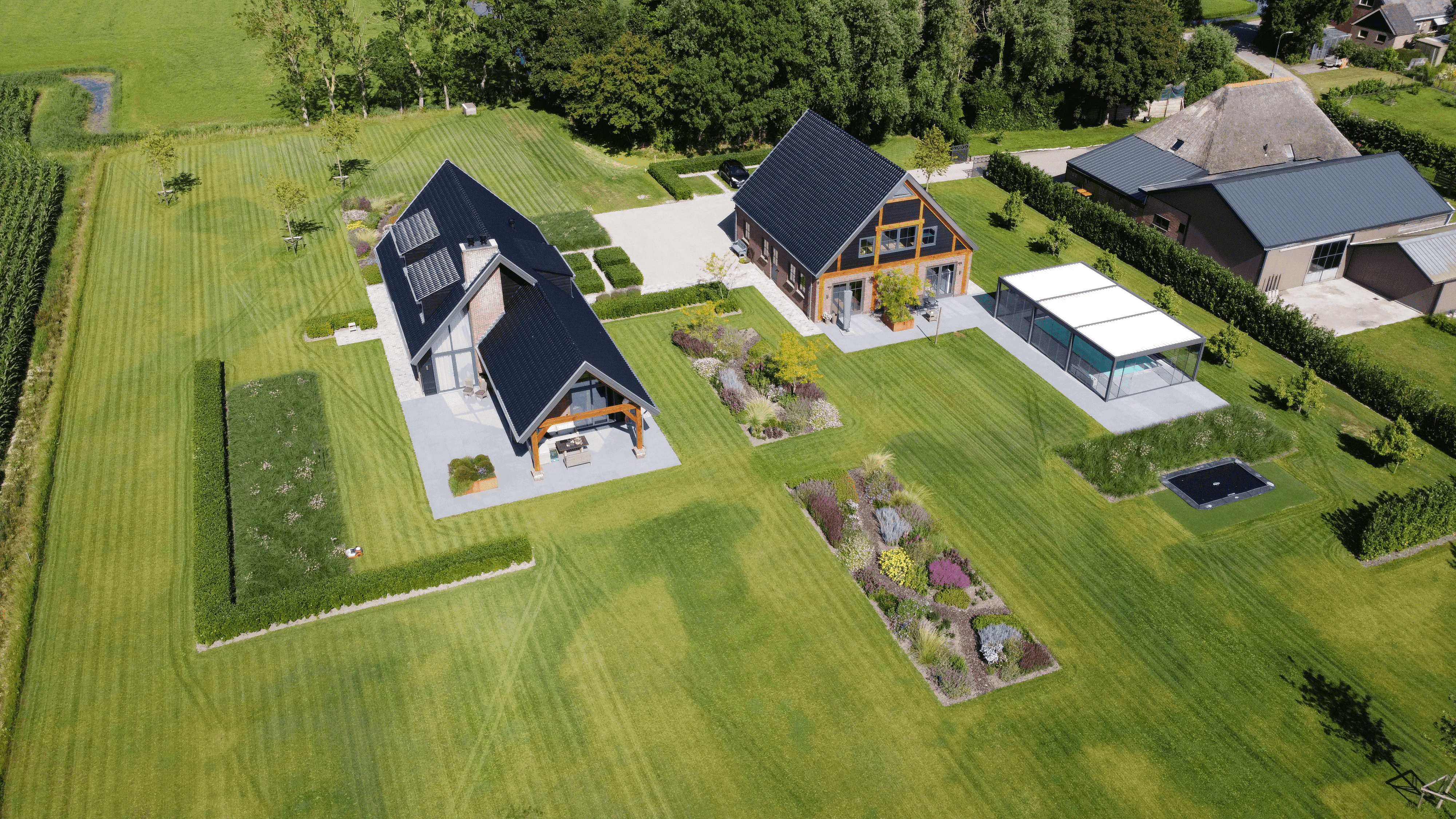 A modern, glass-walled house with warm interior lighting is perched on a rocky cliff overlooking a calm sea at sunset, under a clear blue sky.