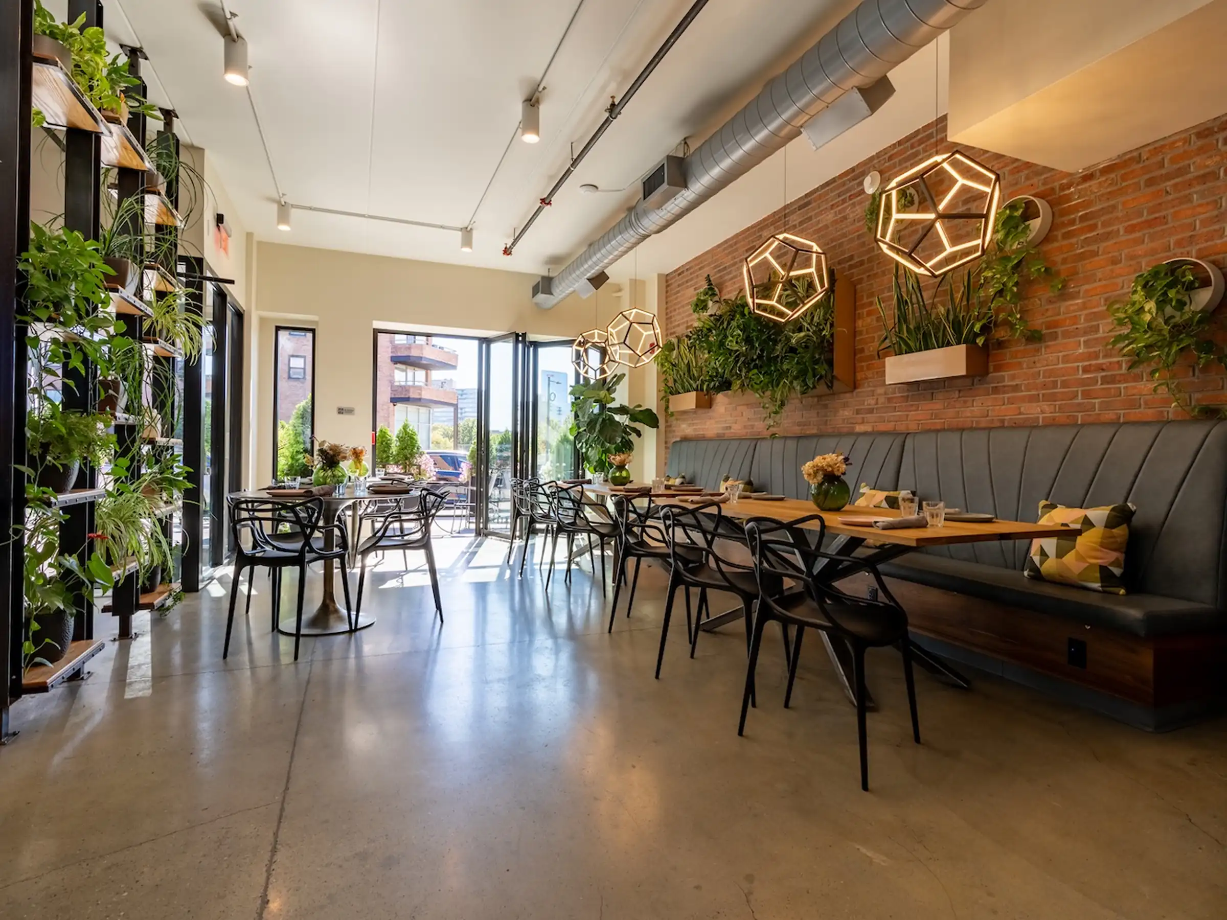 Polished concrete flooring in a modern hotel restaurant with exposed brick, green living walls, geometric pendant lights, and bistro seating.