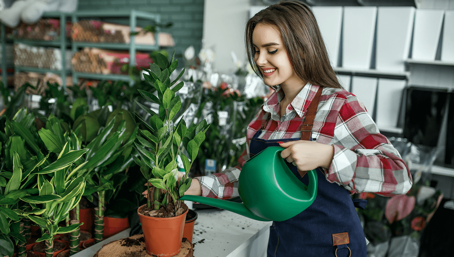 Happy positive young woman working greenhouse enjoying from watering beautiful flowers.