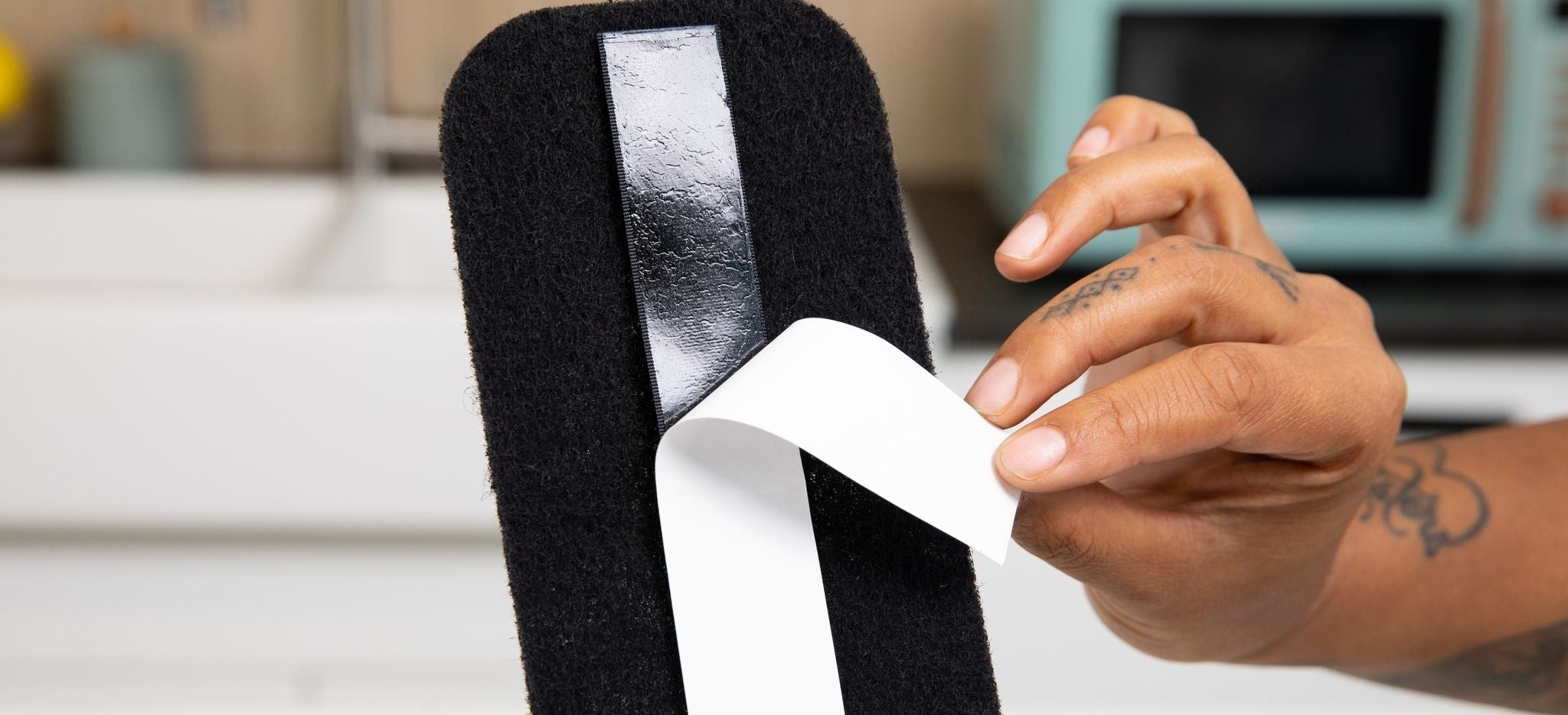 Peeling the paper backing off the adhesive strip on the back of a Barnakl pad.
