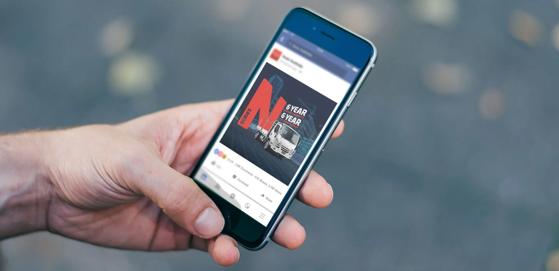 Hand holding a phone showing an Isuzu N Series Facebook post with a red N and '6 Year' warranty text