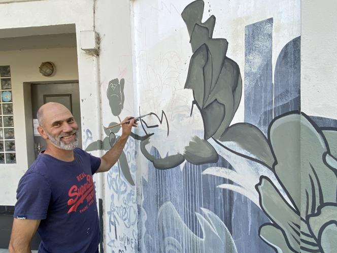 A smiling man paints grey leaves onto a wall beside a doorway.