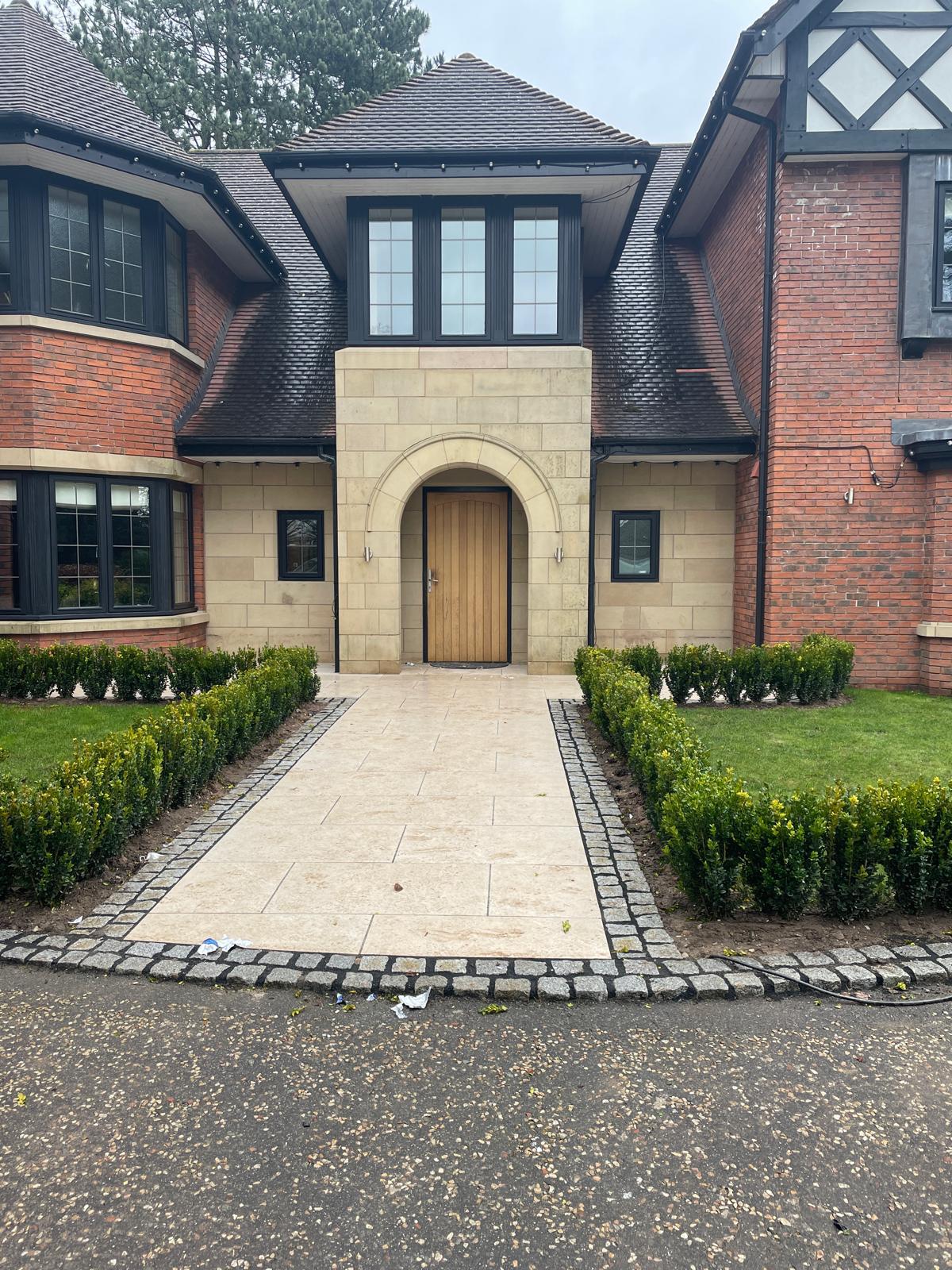 LK Landscaping and Groundworks project: Elegant front garden design featuring stone paving, cobblestone edging, and manicured box hedges. Showcasing expert hardscaping and landscaping for luxury Cheshire home with brick and stone facade.