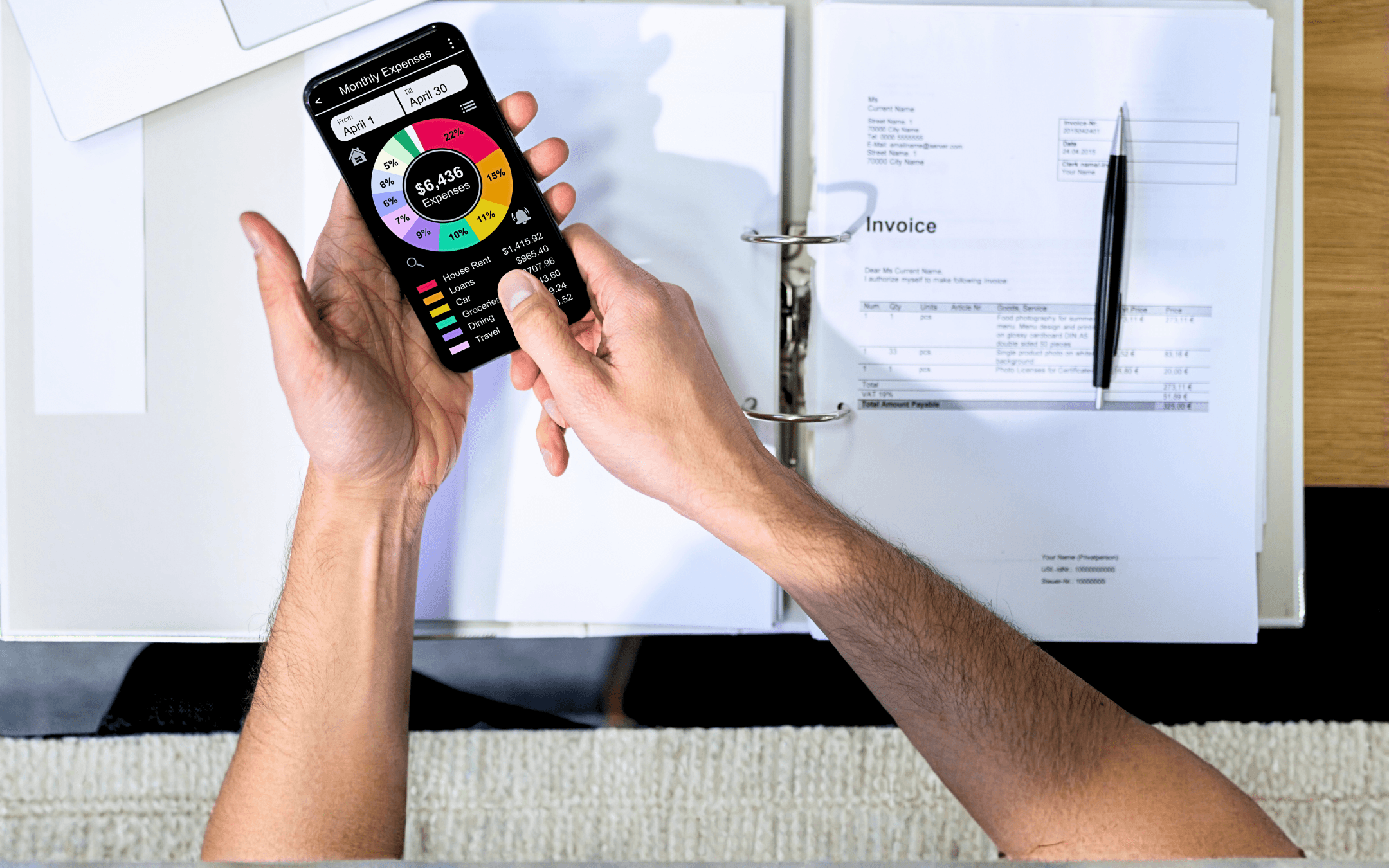 Person holding phone displaying a pie chart of a business plan with documents, and pen in a binder.