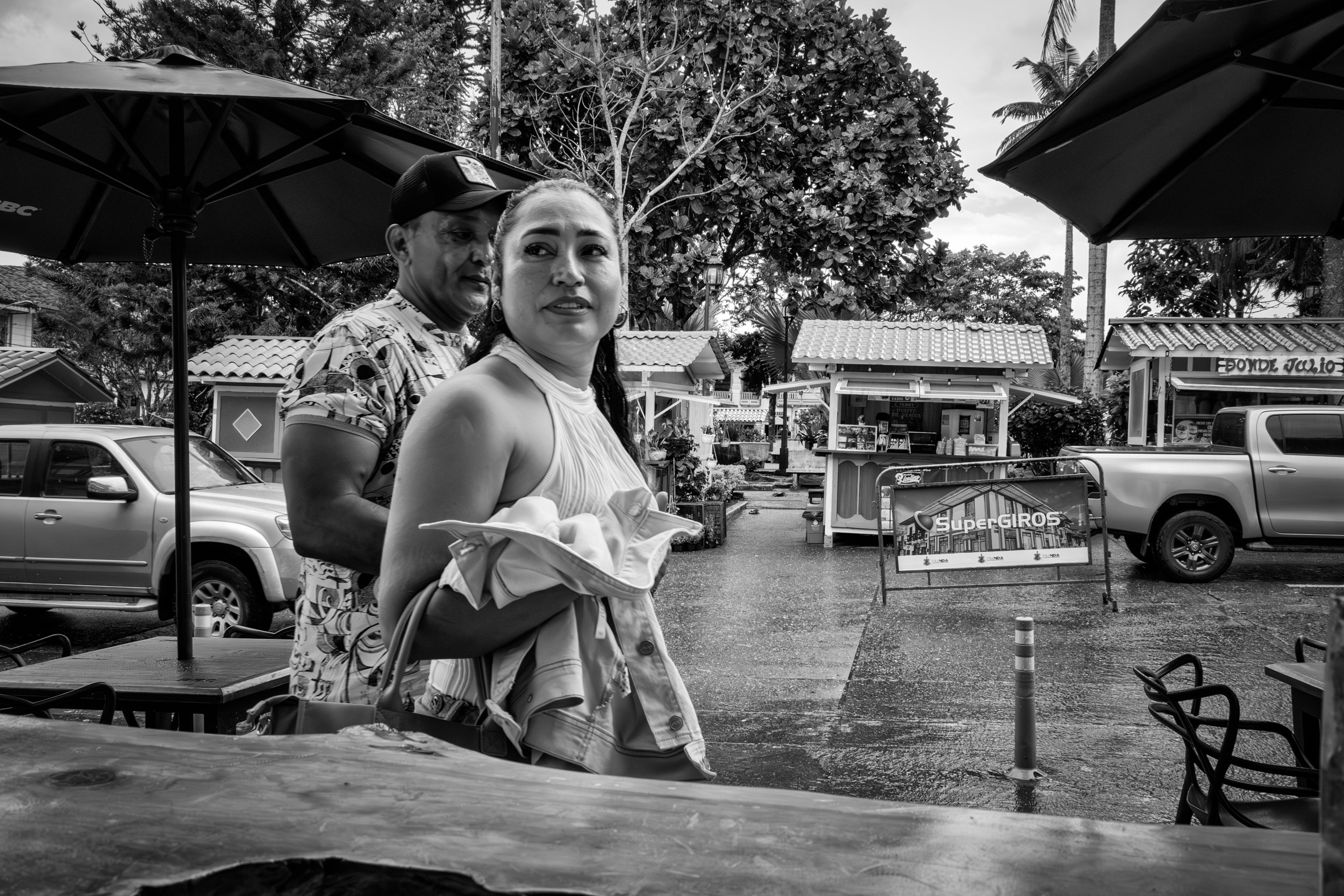 Rainy street scene with people passing by a bar window.