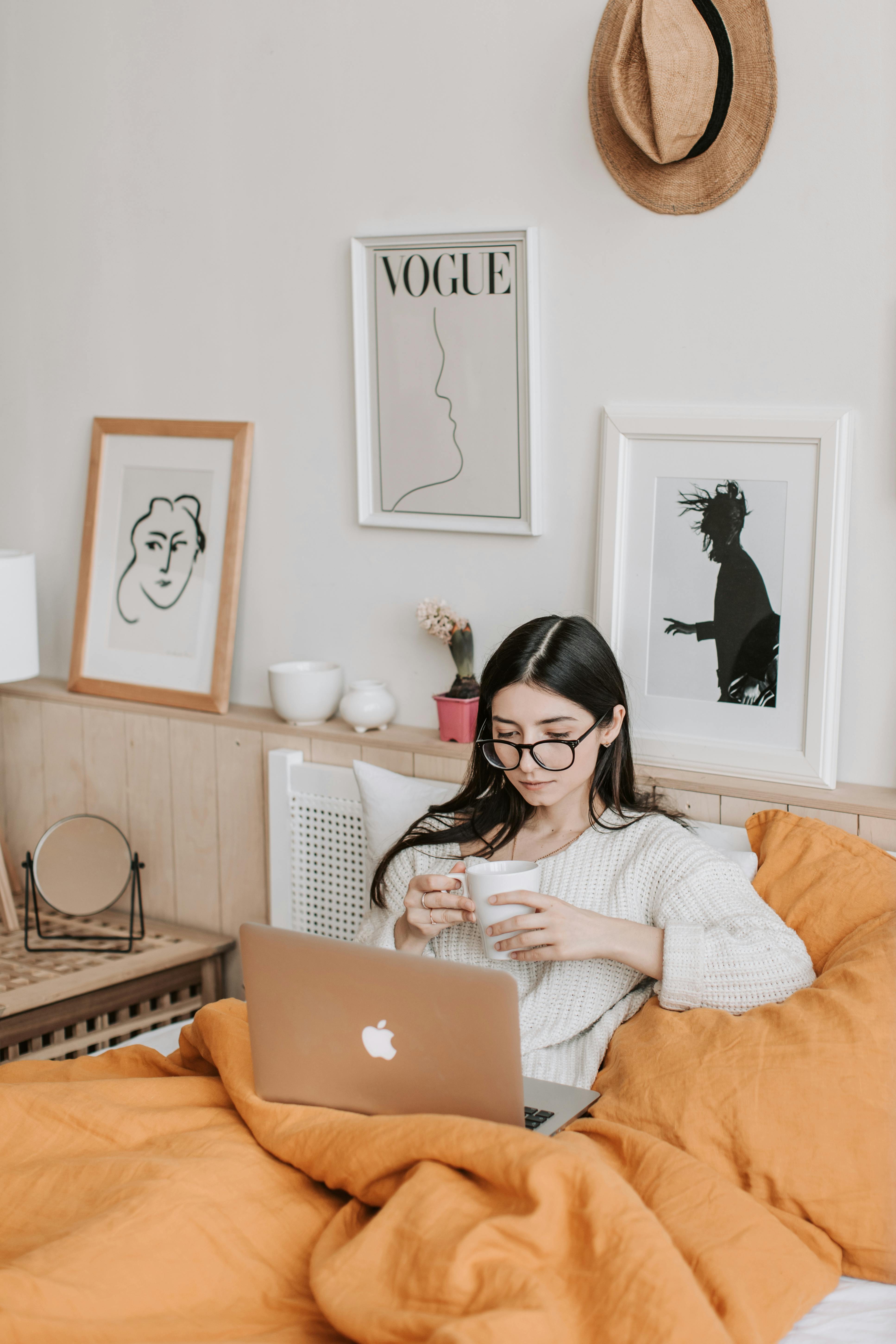 Woman Having Coffee And Using Laptop In Bed while reading a book