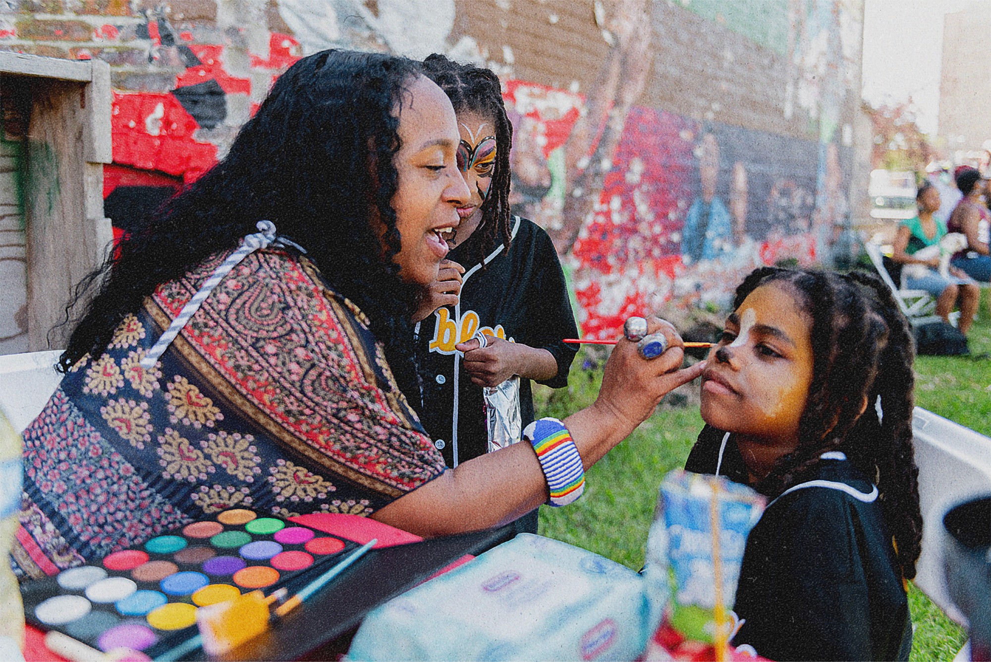 A woman is painting the face of a child at a community event.
