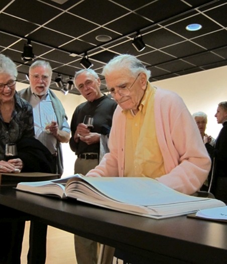 A group of old people staring at a design book on a table.