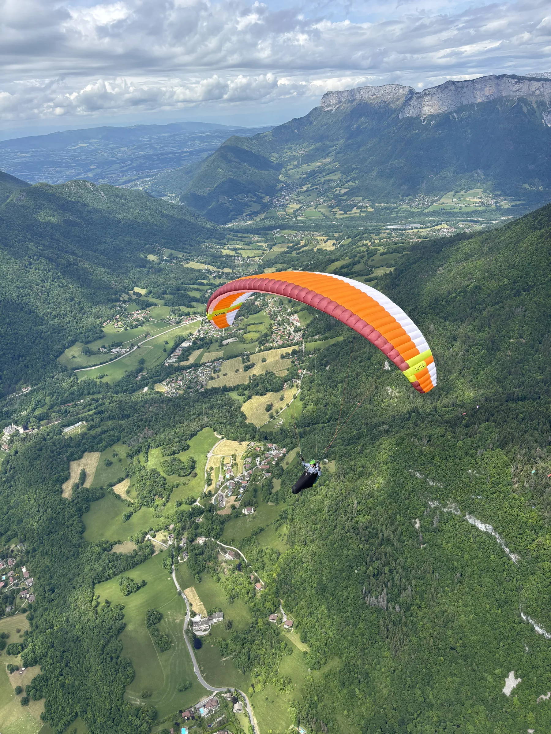 Orange paraglider flying close above a green Alpine valley