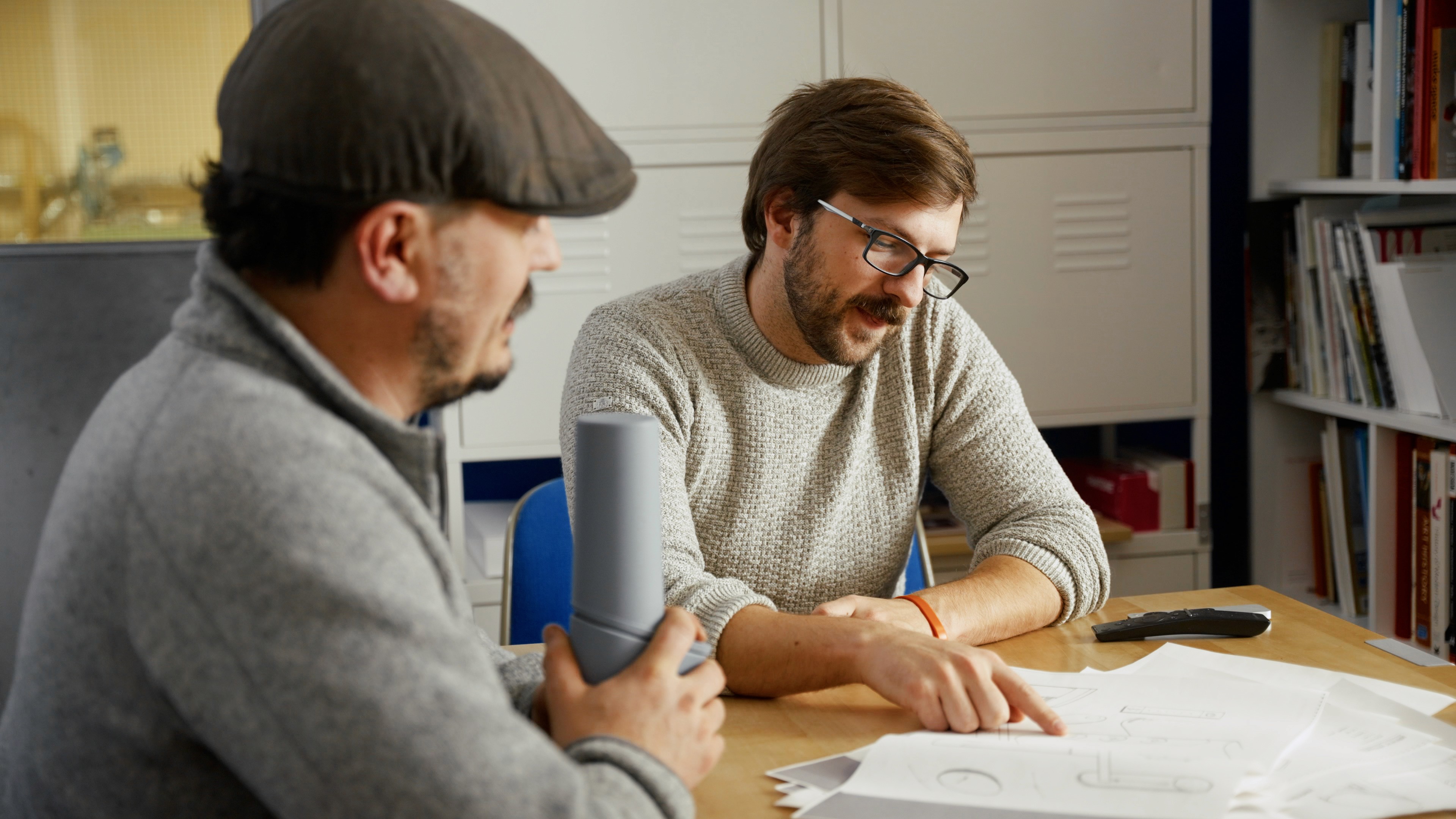 Two men discuss some drawings of a product protype in a boardroom environment