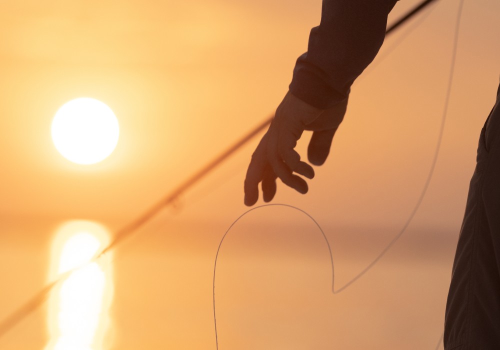 Closeup of a hand pulling the fly line with a golden sunset in the background