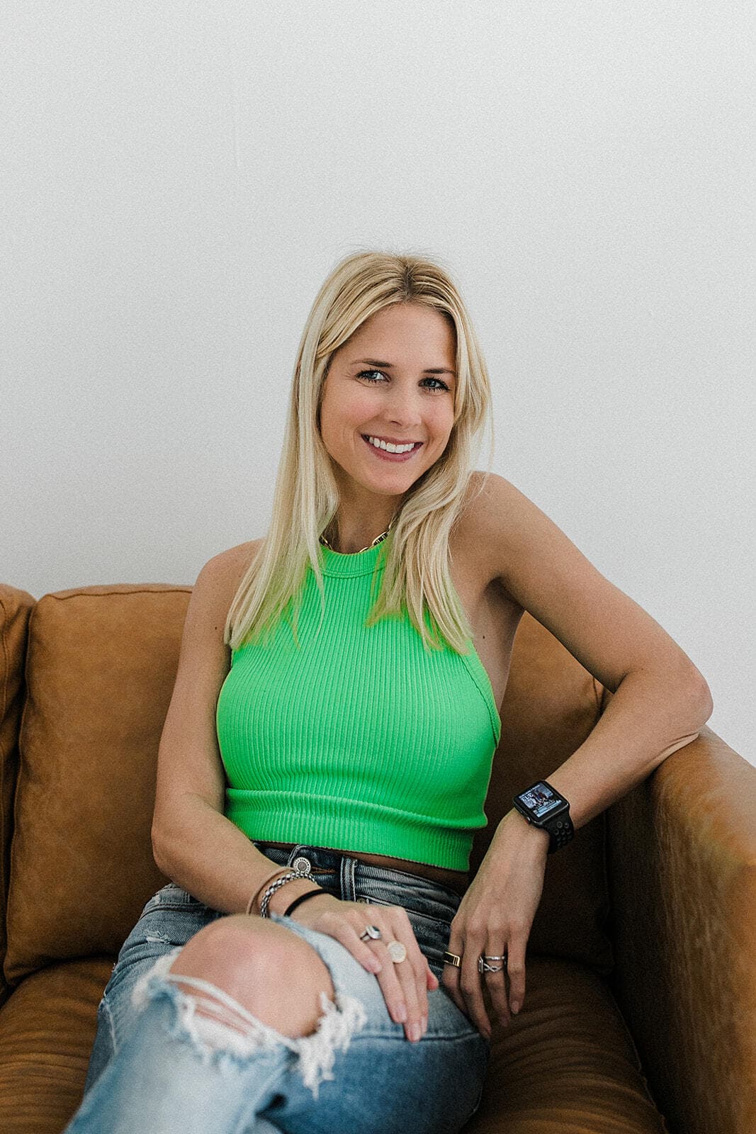 A model in a bright green top smiles while seated on a stylish couch at Revelator Studio in Shreveport, a natural light photography studio perfect for creative and professional photoshoots.