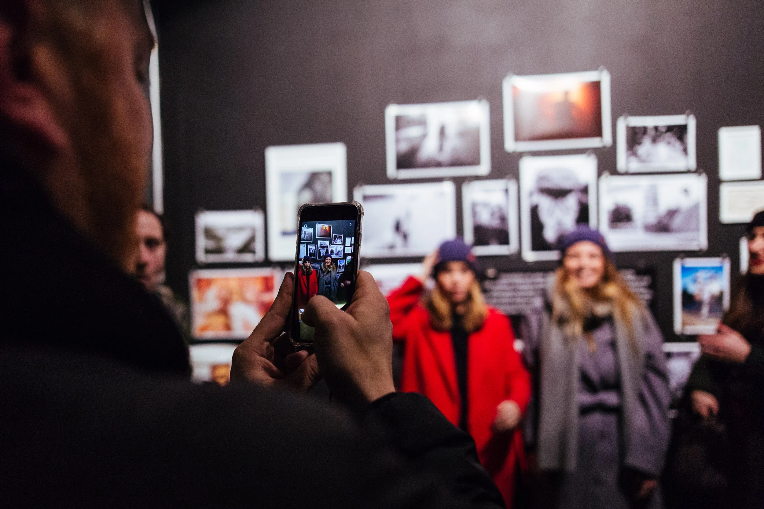 Visitor photographing two guests with a smartphone in front of the black photo wall at the BRIXTON pop-up event.