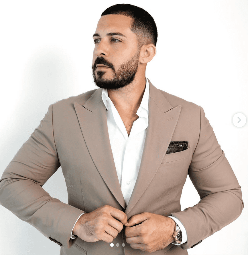 Smiling woman in beige yoga outfit sitting in natural light with green plants in the background.