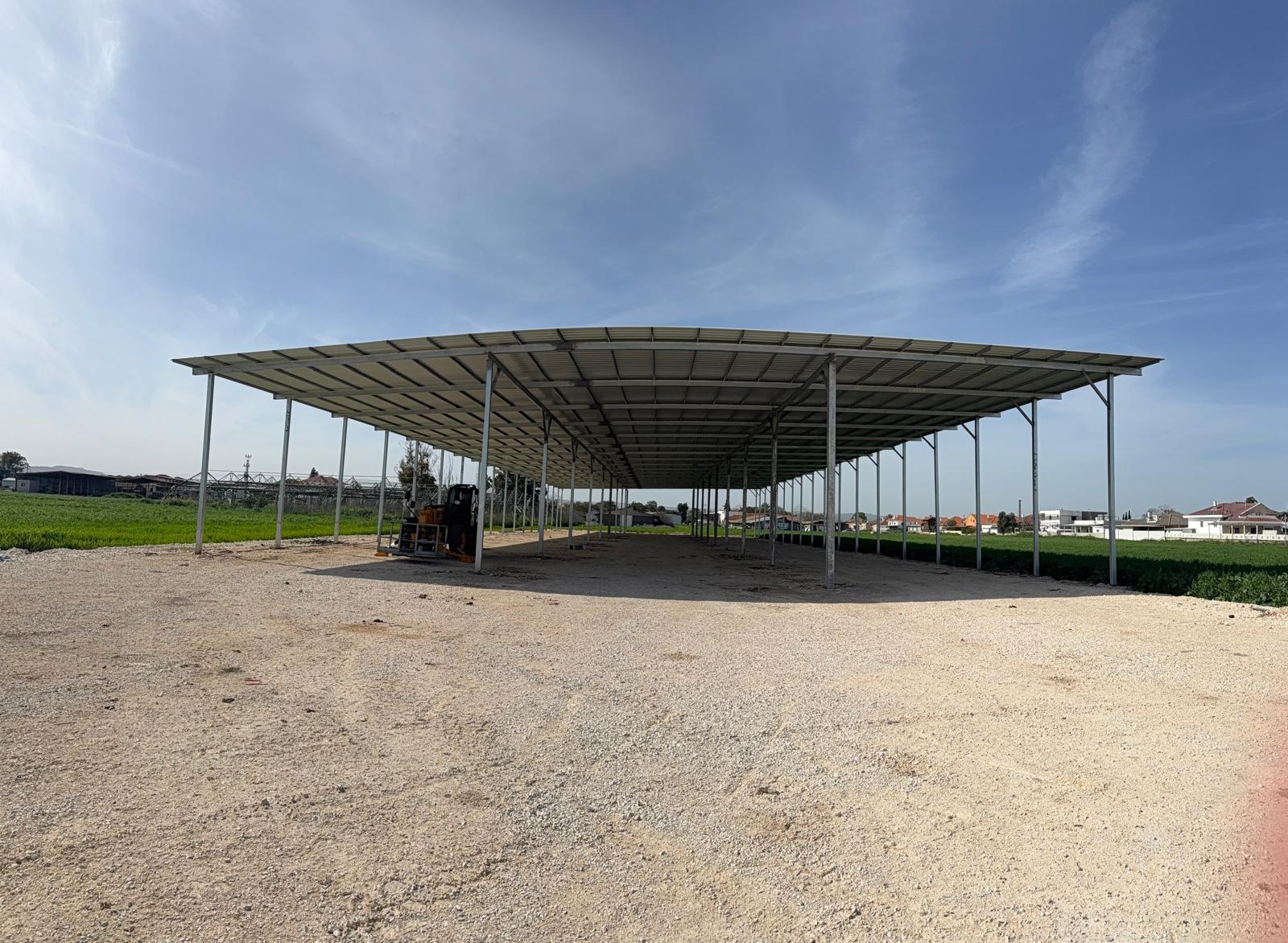 A modern, glass-walled house with warm interior lighting is perched on a rocky cliff overlooking a calm sea at sunset, under a clear blue sky.