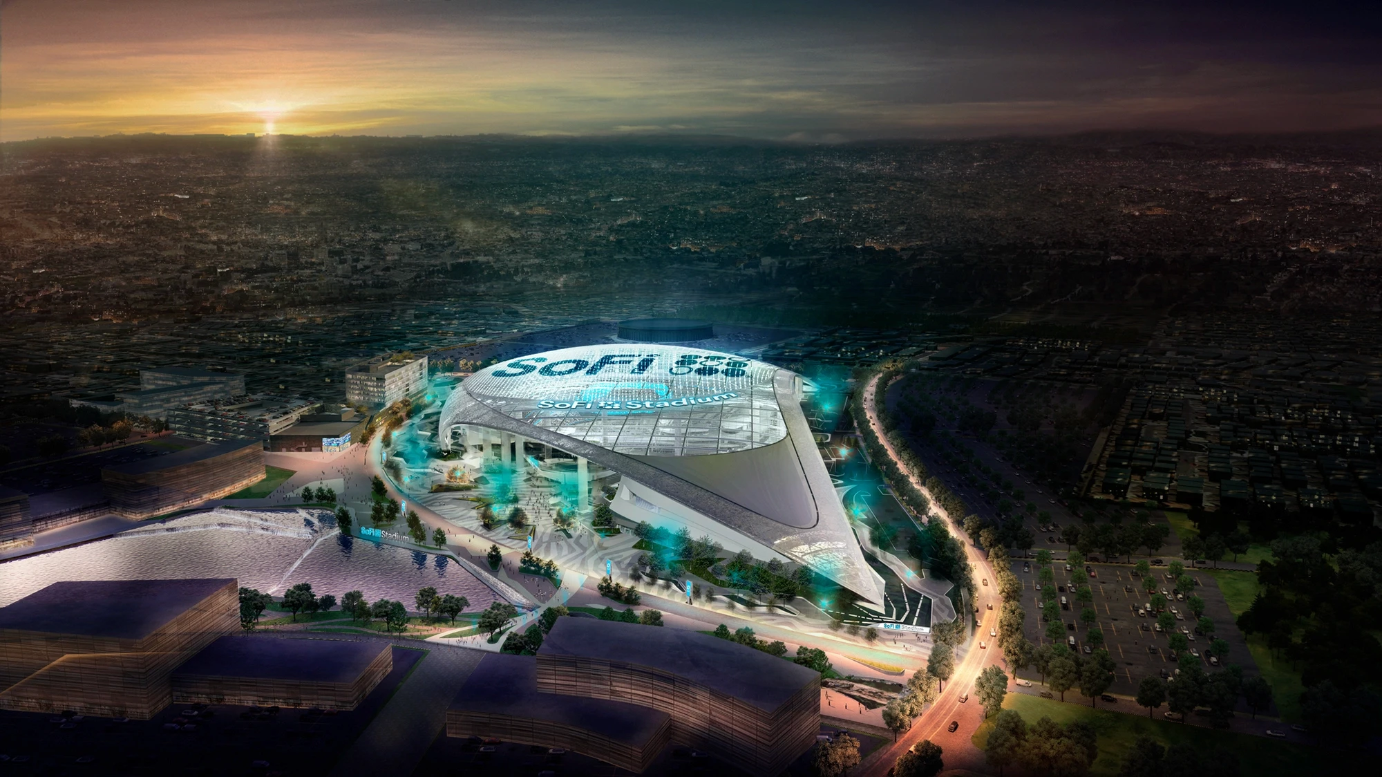 Aerial night view of SoFi Stadium illuminated with blue lighting and cityscape in the background.