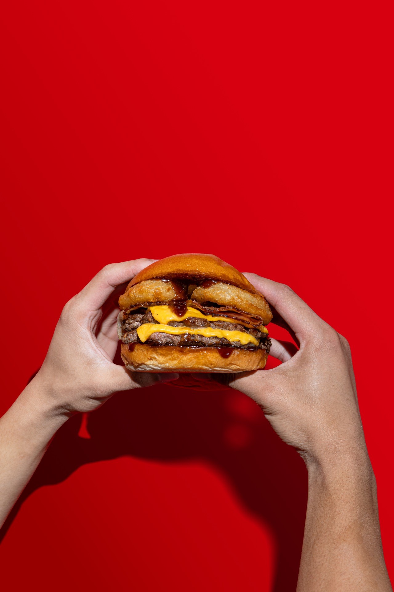 Hands holding a cheeseburger against a red background
