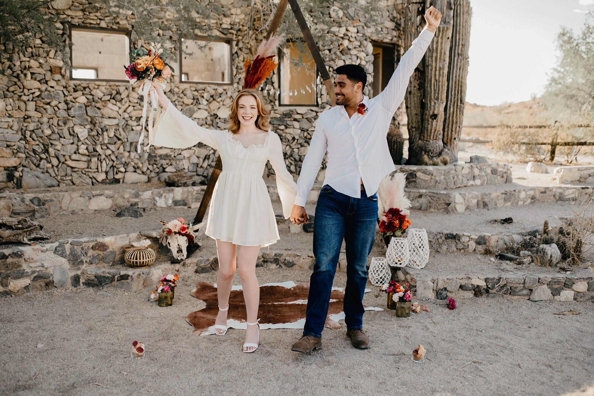 A couple joyfully celebrates in front of a rustic stone building.