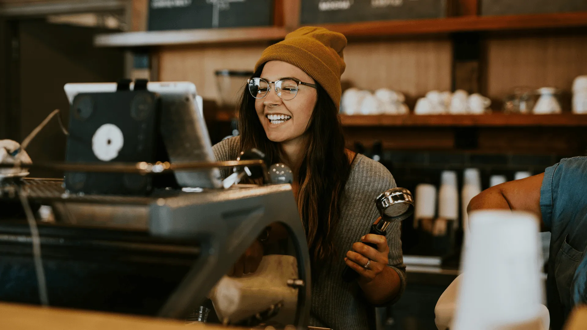 A female barista smiling behind a coffee machine in a cafe