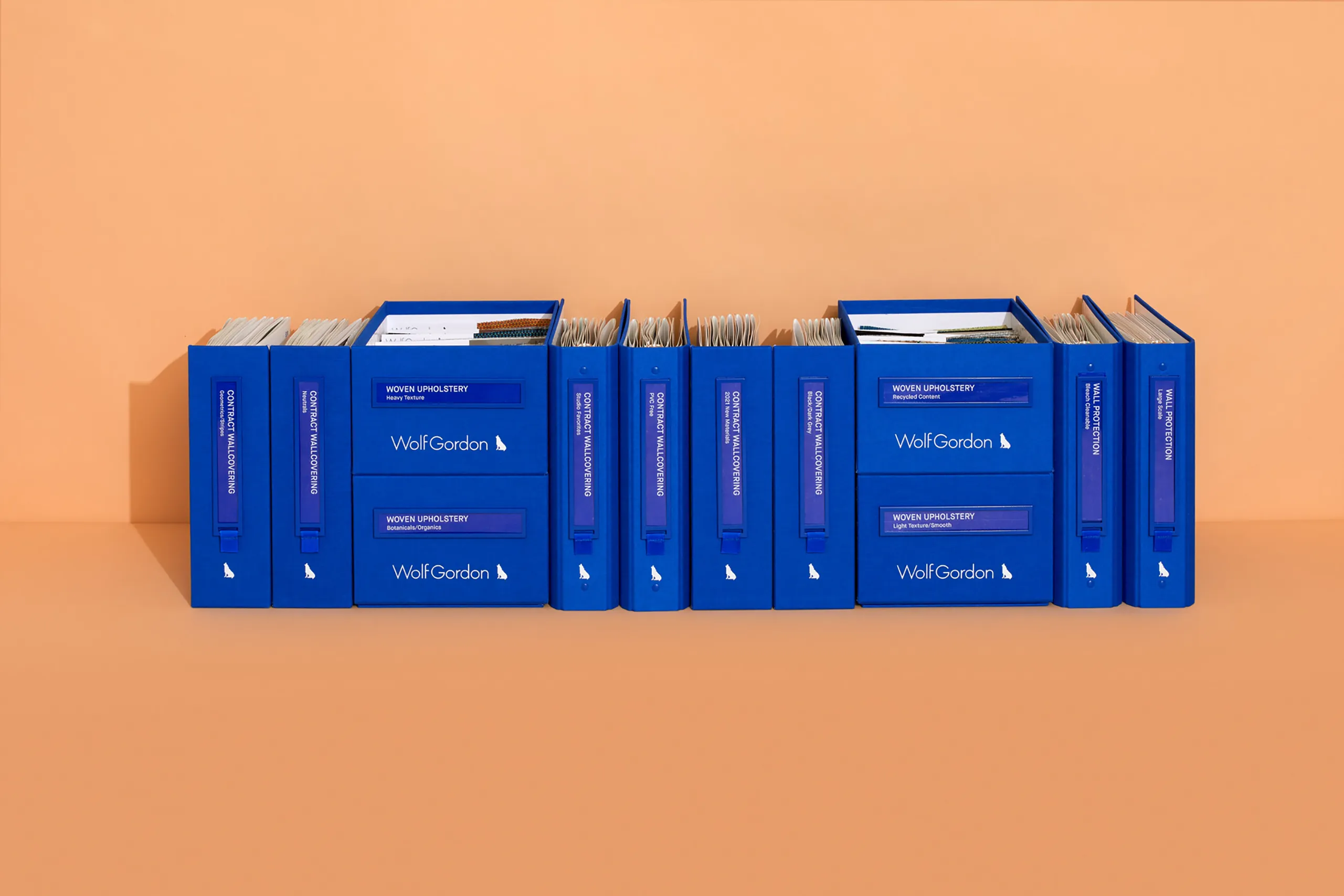 Blue Wolf-Gordon material sample binders and organizers arranged on an orange background