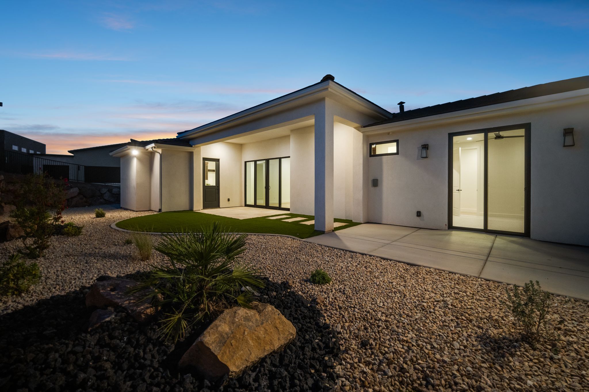 Back exterior of The Overlook at Falcon Ridge at twilight, Hurricane, Utah, showcasing large windows and patio lighting.