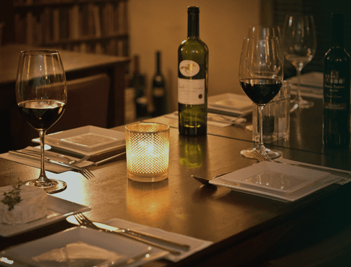 A cozy dining setup with a bottle of wine, glasses, and a lit candle on a wooden table.