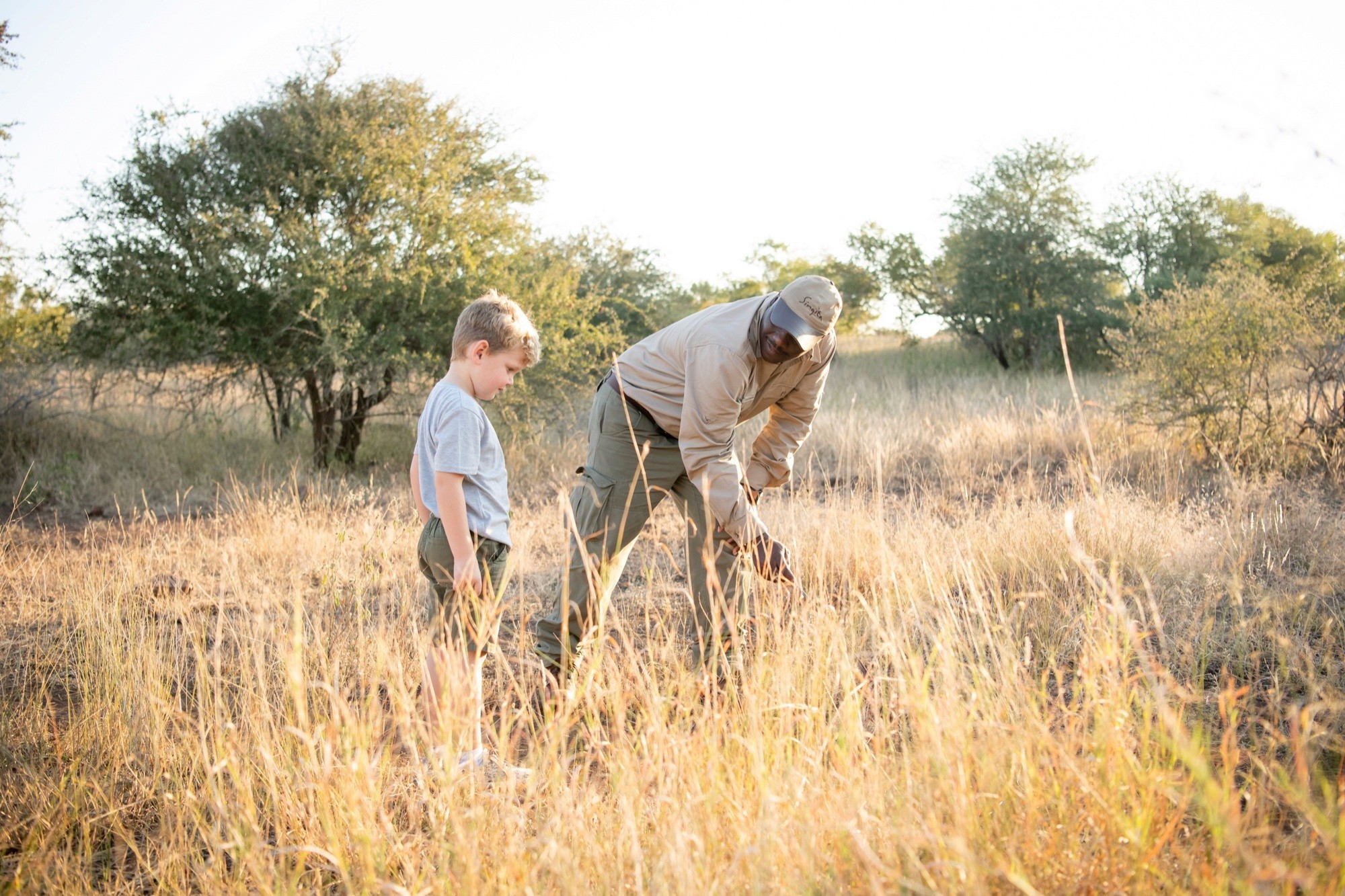 A young boy learning tracking beside his guide in tall grass