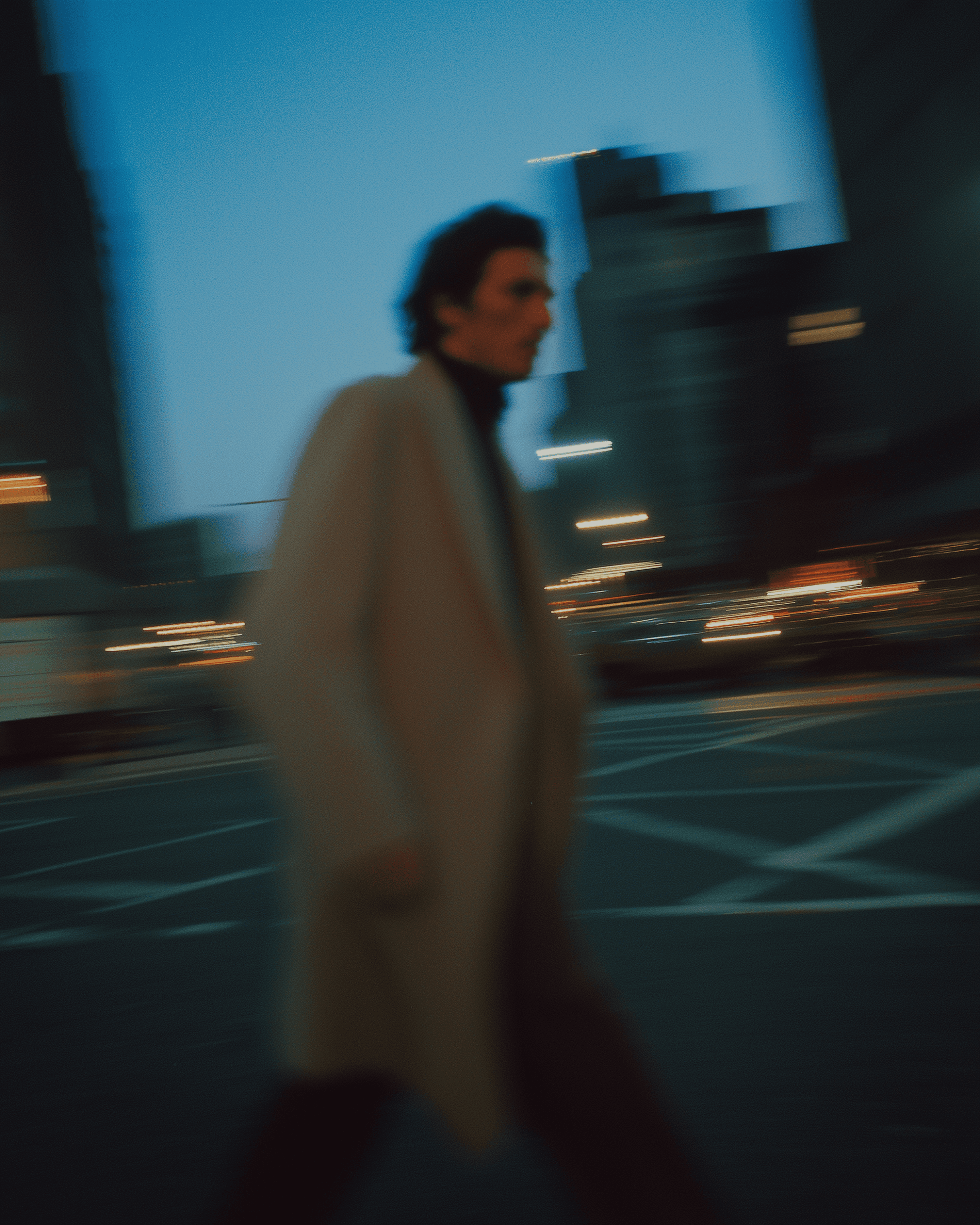Motion-blurred man walking in a city at dusk with urban lights and skyscrapers, cinematic street photography with long exposure effect.