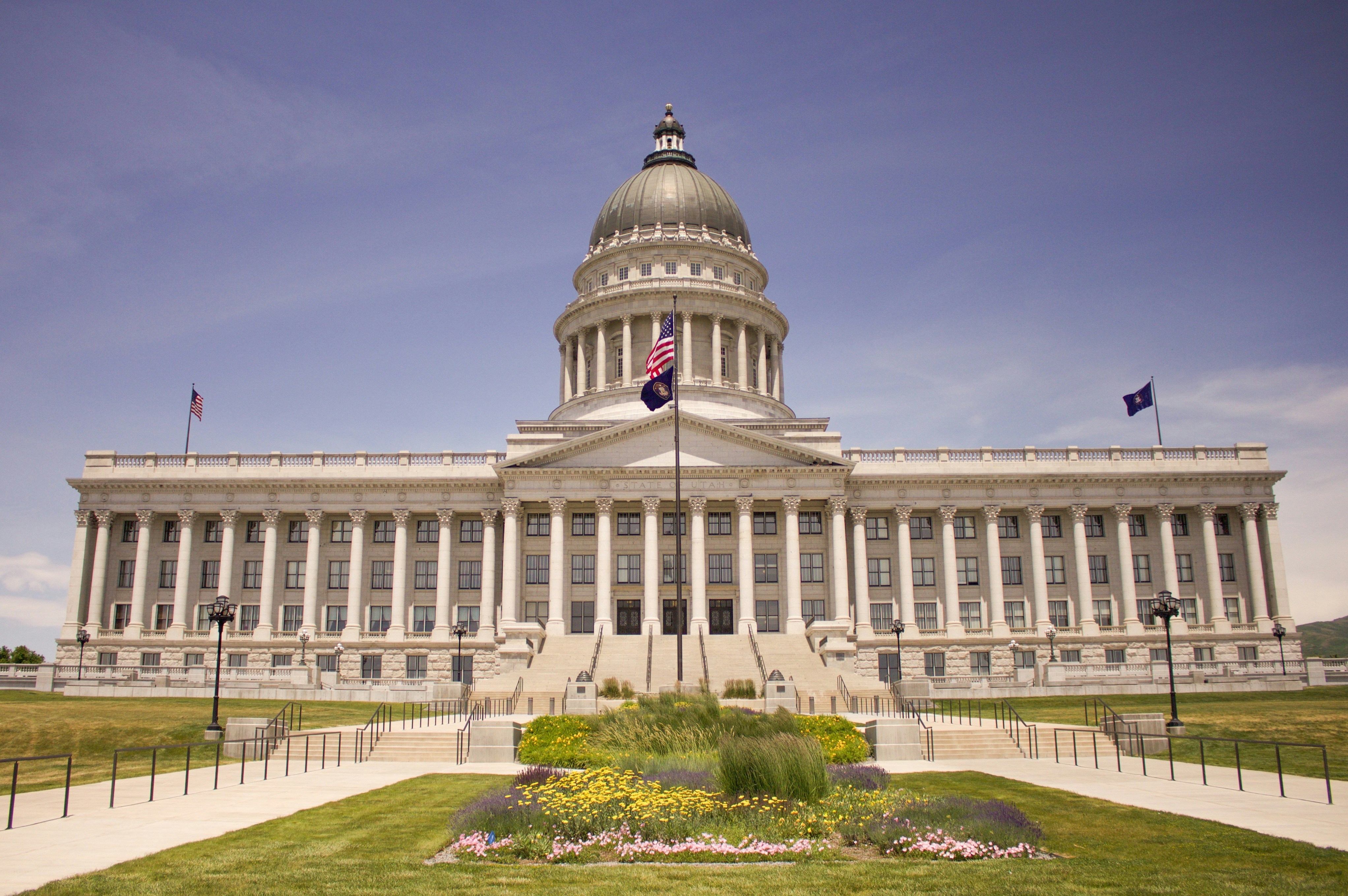 Utah State Capitol building in Salt Lake City with its iconic dome and neoclassical architecture, featuring manicured gardens and stone steps leading to the entrance under a purple-tinted sky