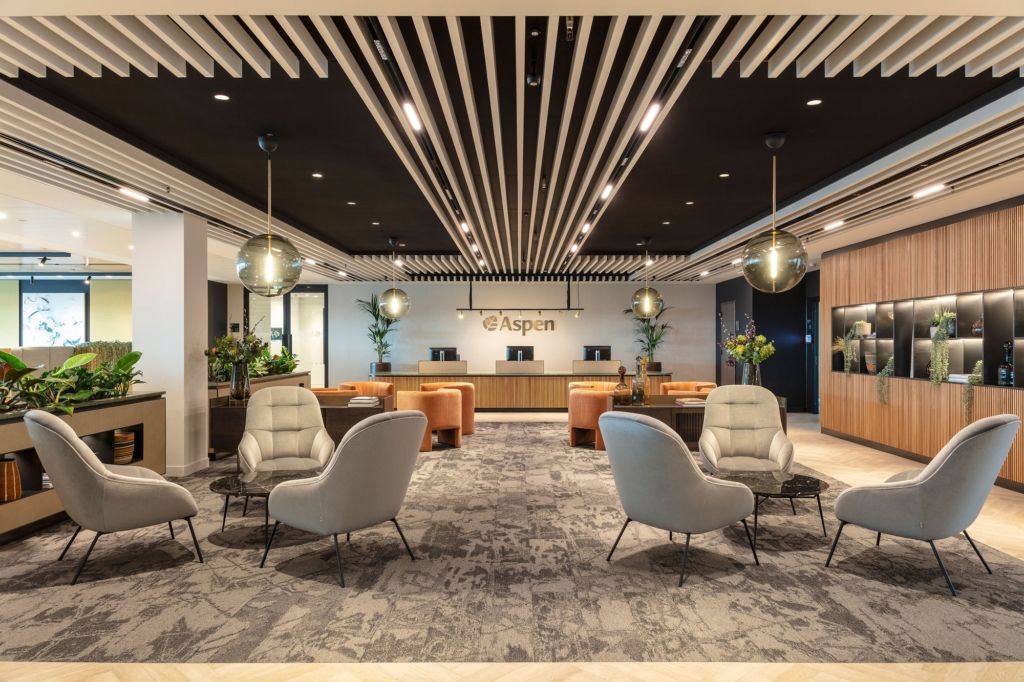 A luxurious and spacious corporate office reception in Bengaluru by Zepspace, featuring an architectural slatted ceiling with integrated lighting and multiple plush guest seating areas