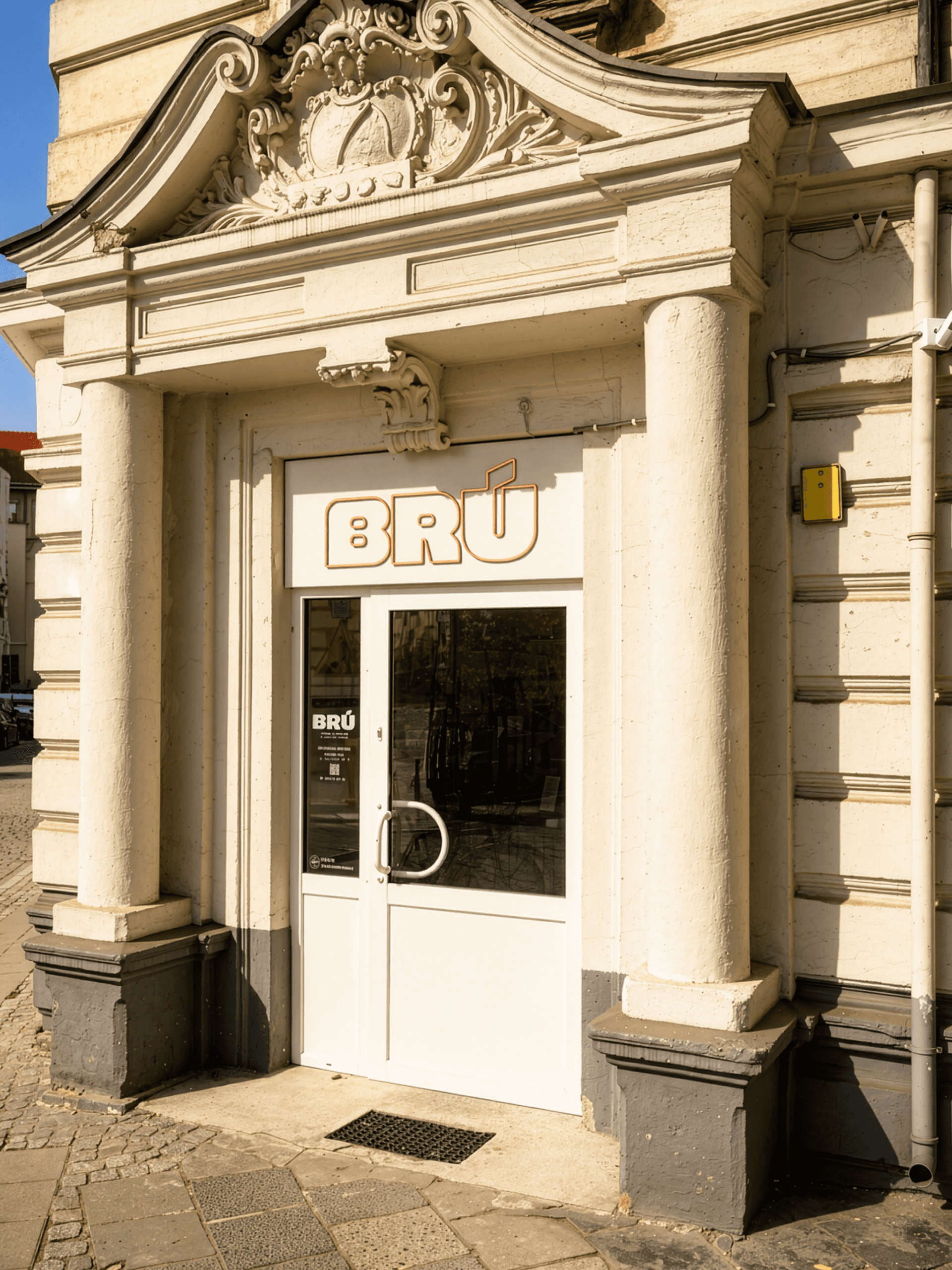 BRÚ café entrance with logotype on glass door and pastry display inside, coffee shop brand identity