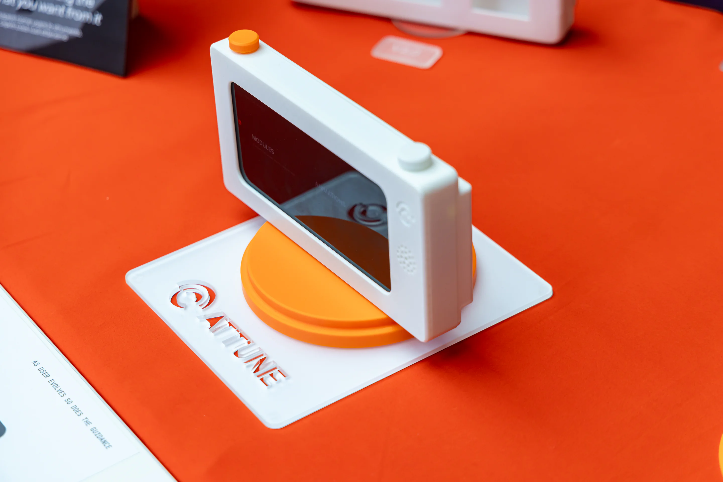 A white Attune camera prototype stands on an orange display base on the exhibition table.