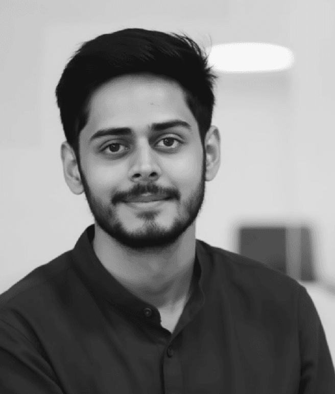 Smiling young man with short hair poses against a dark background, wearing a green button-up shirt.