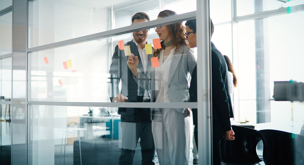 Team members placing colorful sticky notes on a glass wall during a collaborative workshop session