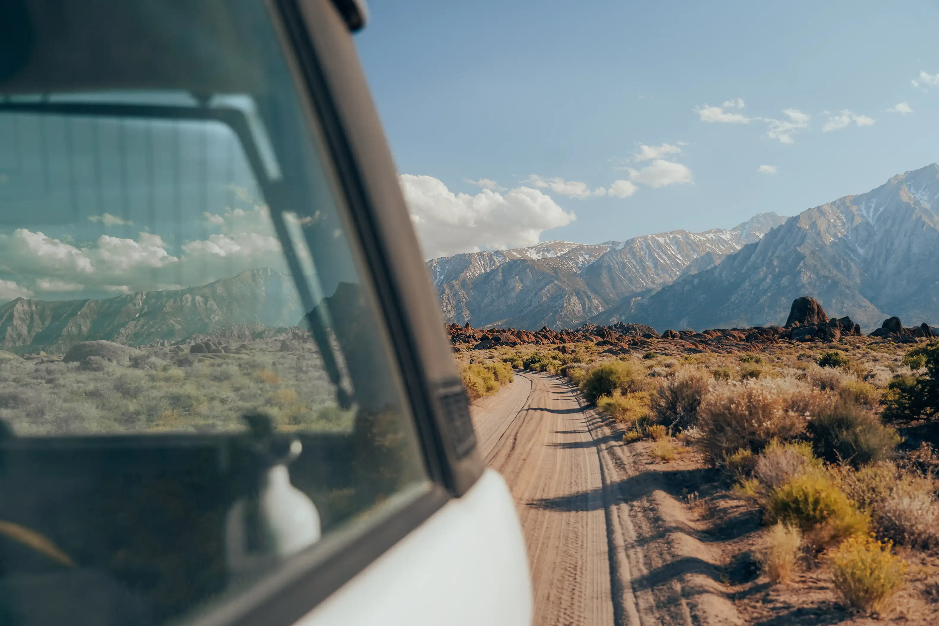 A silver Range Rover SUV driving down a dirt road with mountains in the distance.