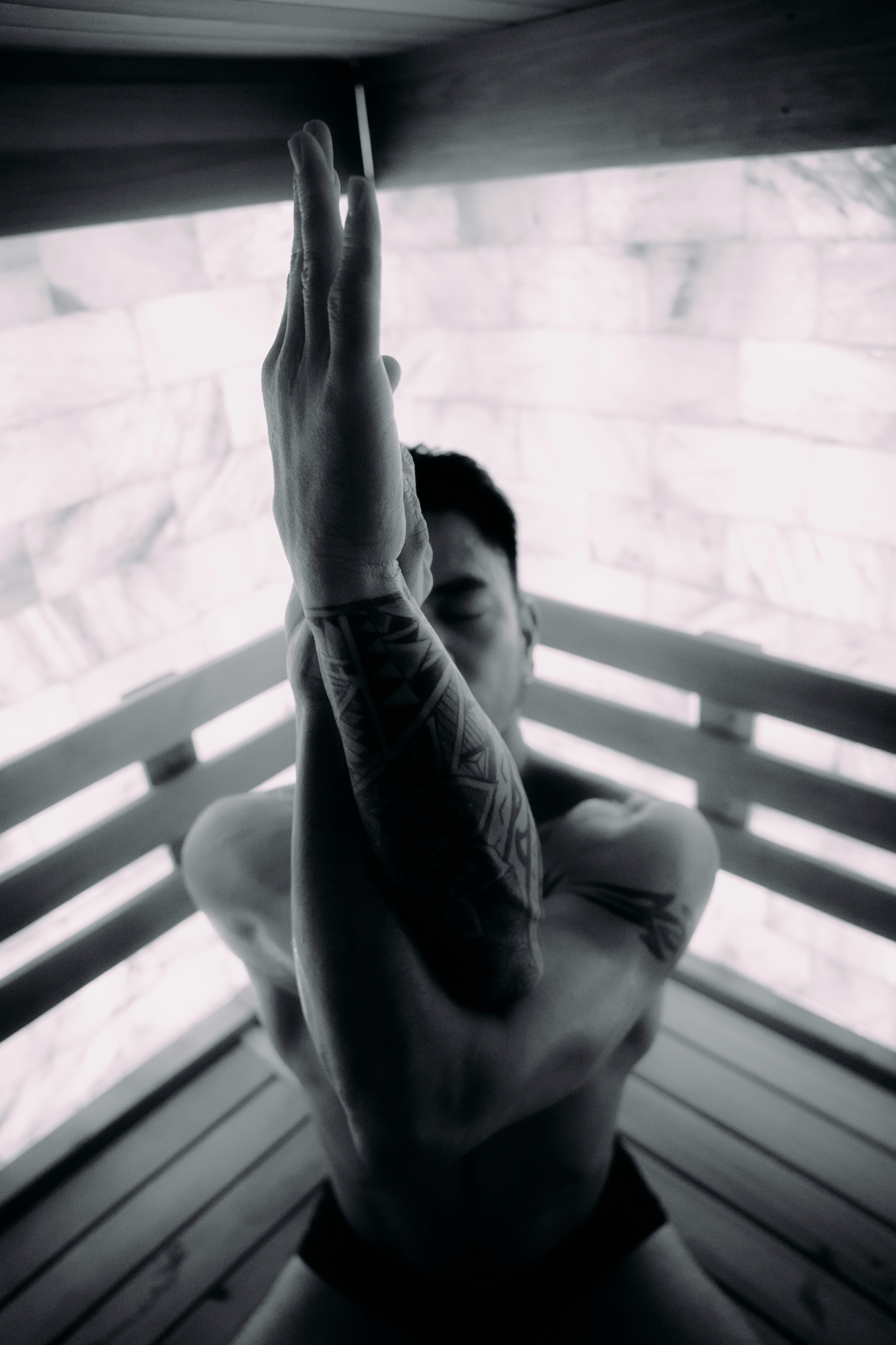 Person seated inside a sauna with arms reaching upward in a quiet stretch, body settling into the heat