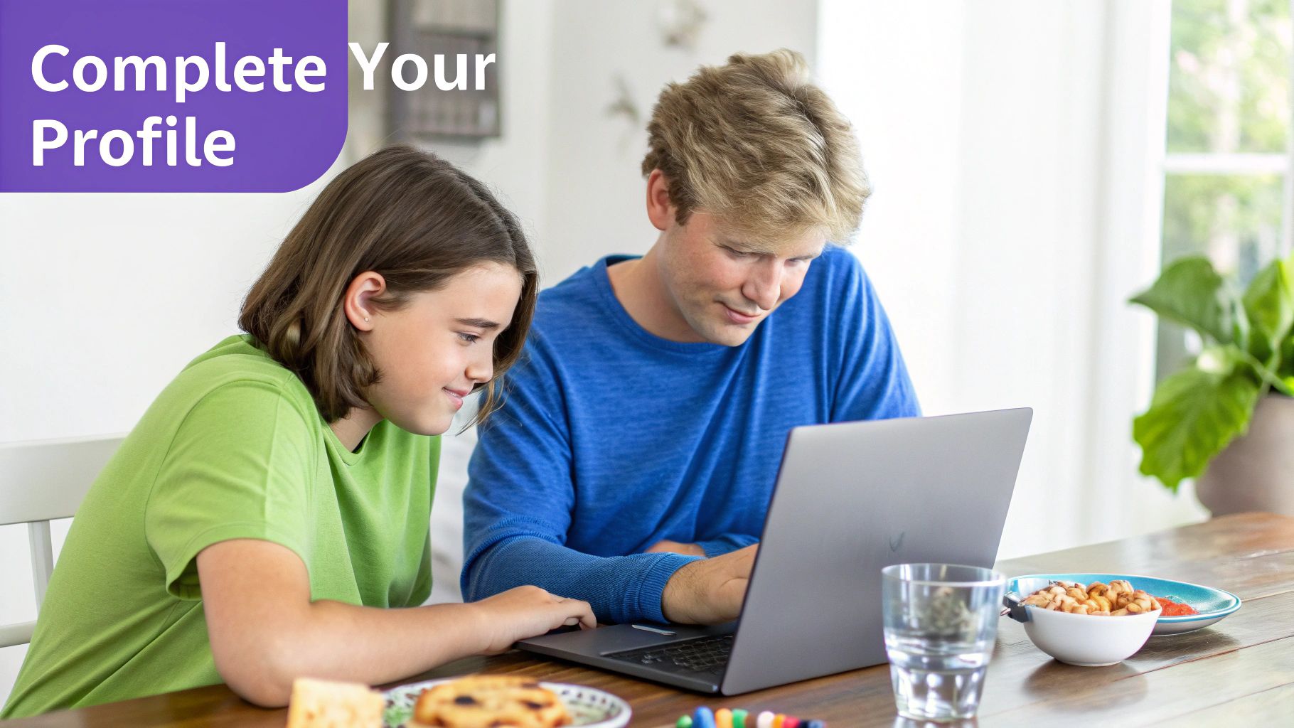 Two young people collaboratively using a laptop at a table with snacks and drinks, smiling.