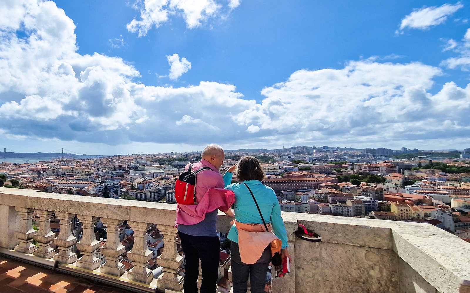 Two people enjoying Lisbon cityscape from Graca Church terrace viewpoint.