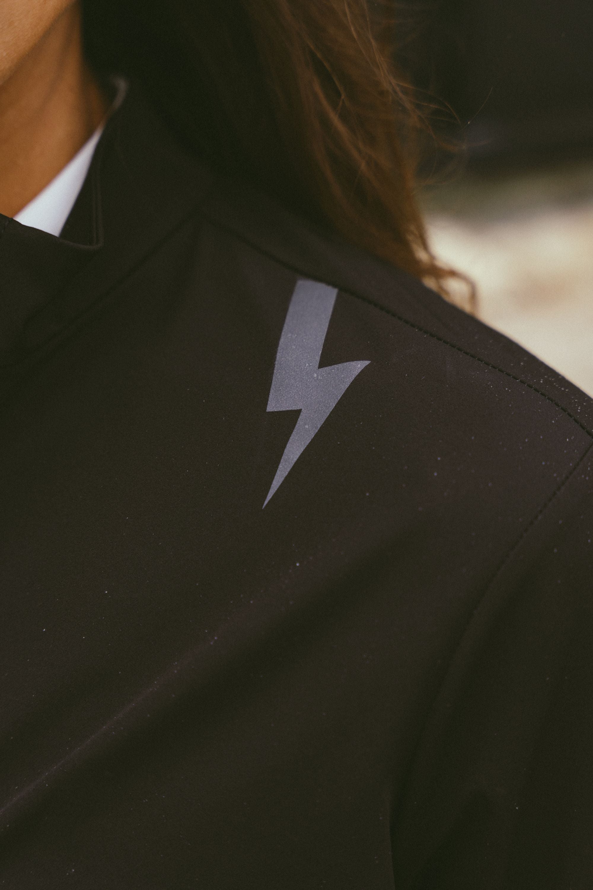 Close-up-detail-of-the-Black-Momentum-jacket-shoulder-highlighting-the-lighting-bolt-sign-and-the-jacket-high-collar