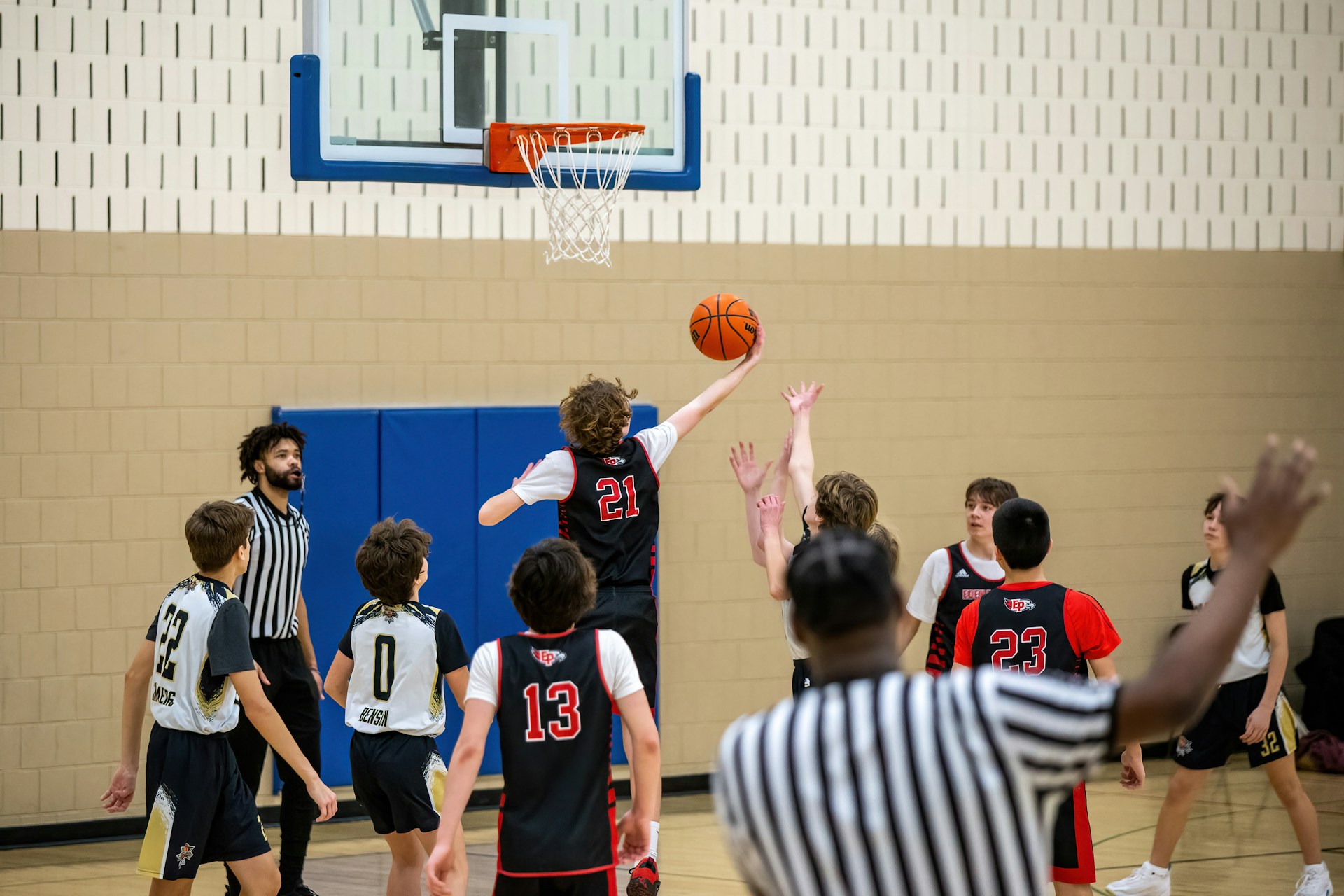 A basketball player in a black #21 jersey goes for a layup while defenders attempt to block.