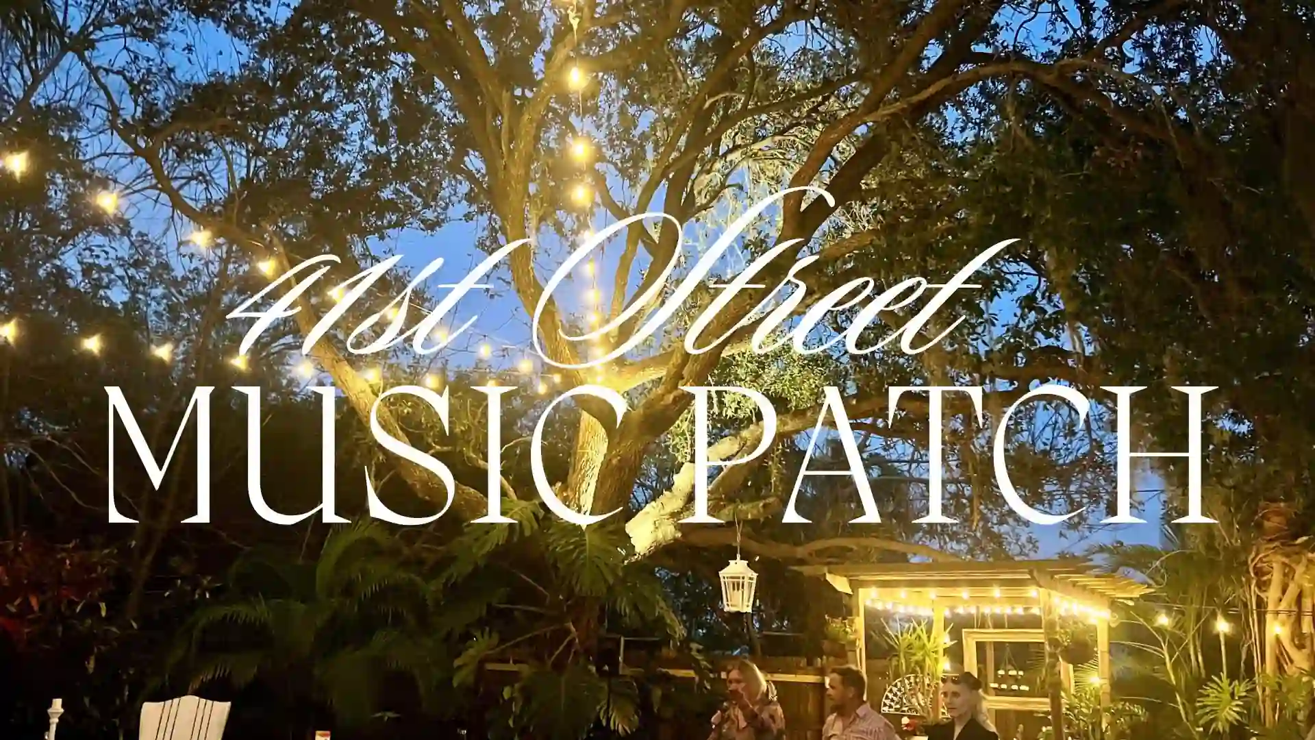 Oak trees with string lights and a lighted stage at 41st St. Music Patch