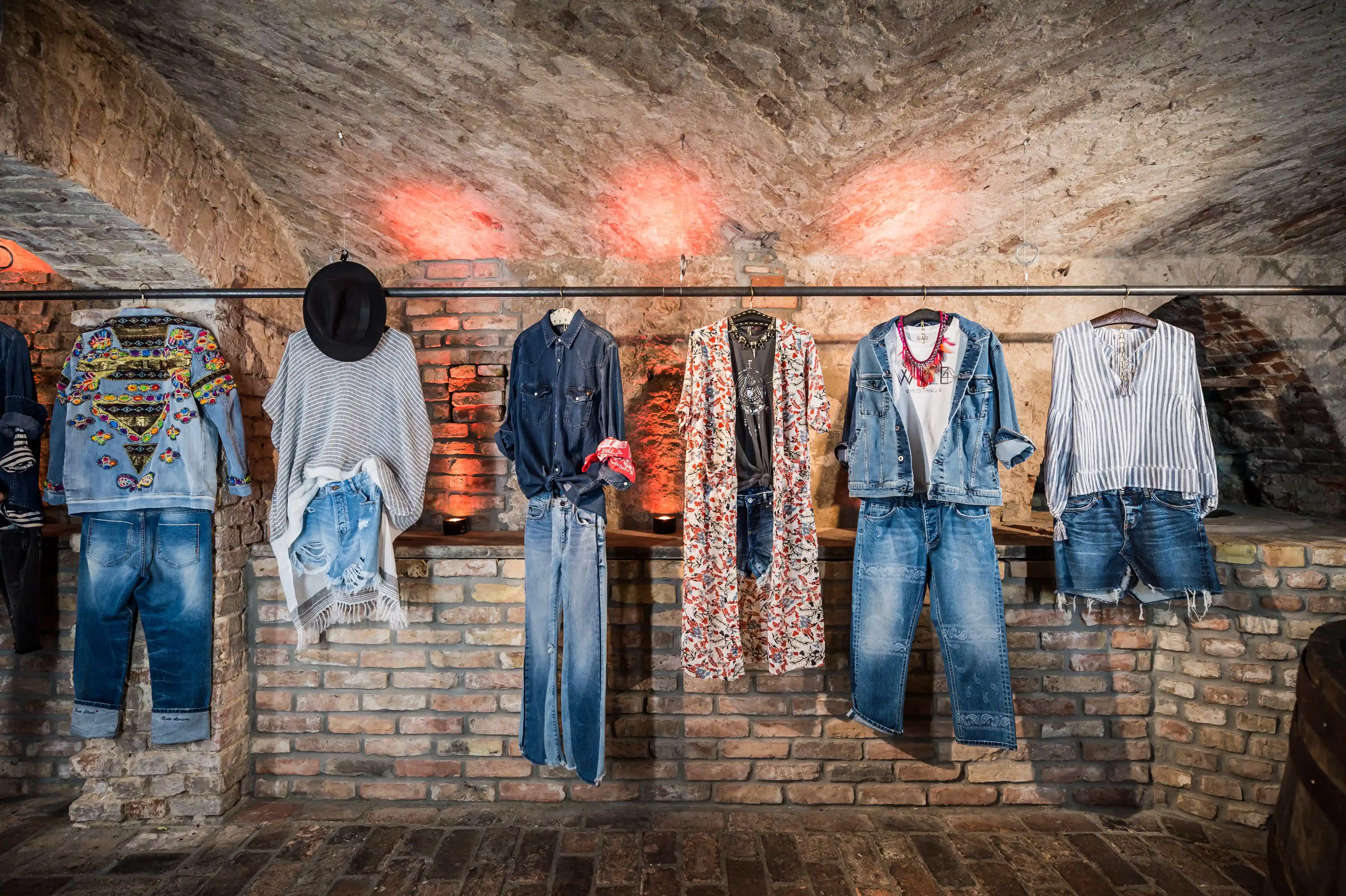 Customized MUSTANG denim collection hanging on a rail in a brick vault with warm red lighting.