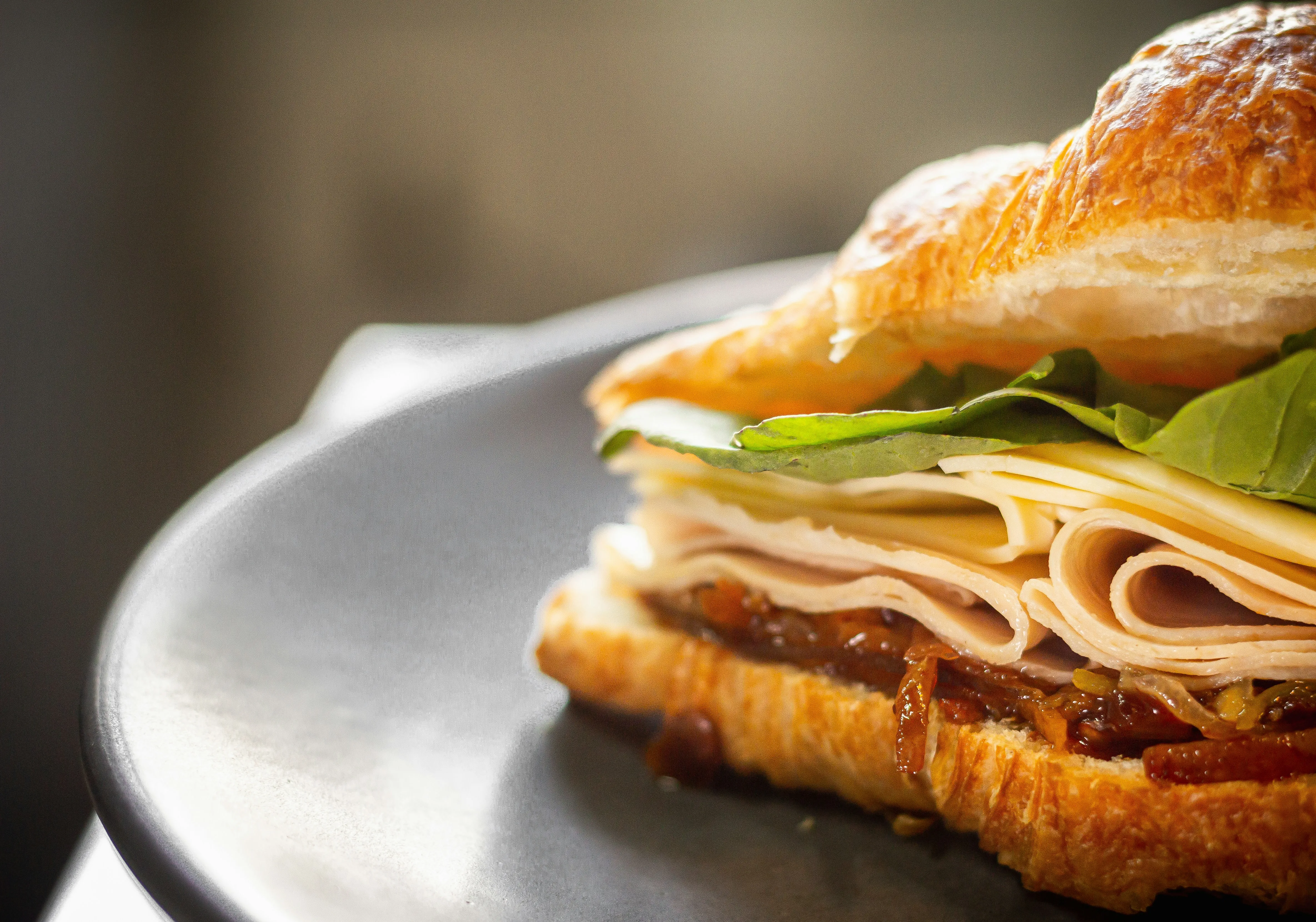 A close-up of a sandwich with turkey, cheese, and greens on a plate, featuring a golden, flaky bread.