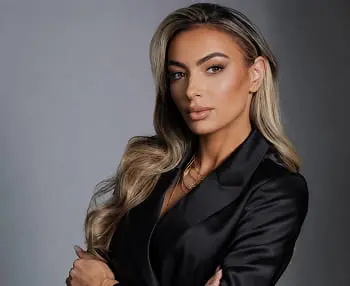Woman with long blonde hair wearing a black blazer against a gray background.
