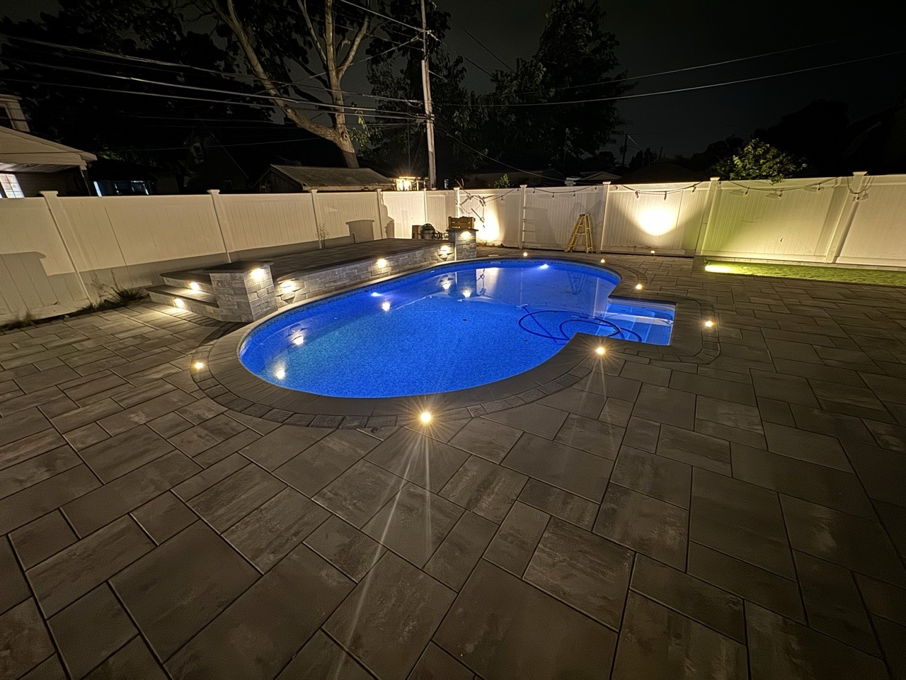 In-ground pool with landscape lighting at night by CMC Masonry