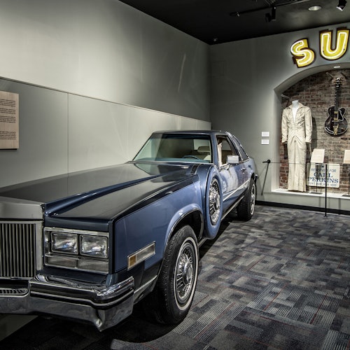 V muzeu je vystaven modrý klasický vůz vedle figuríny v bílém obleku a kytary. Částečně je viditelný neonový nápis "SUN".